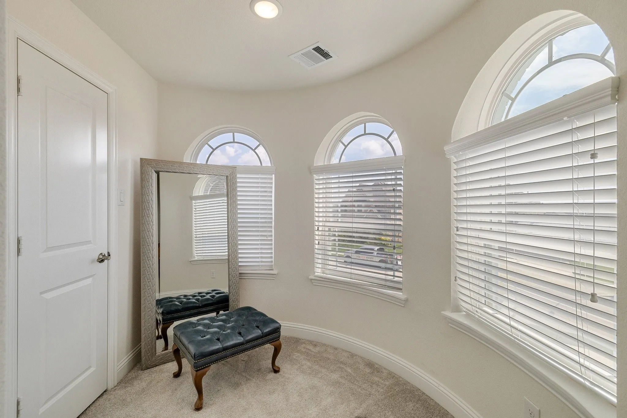 Curved room with carpeted flooring, three arched windows, and recessed lighting