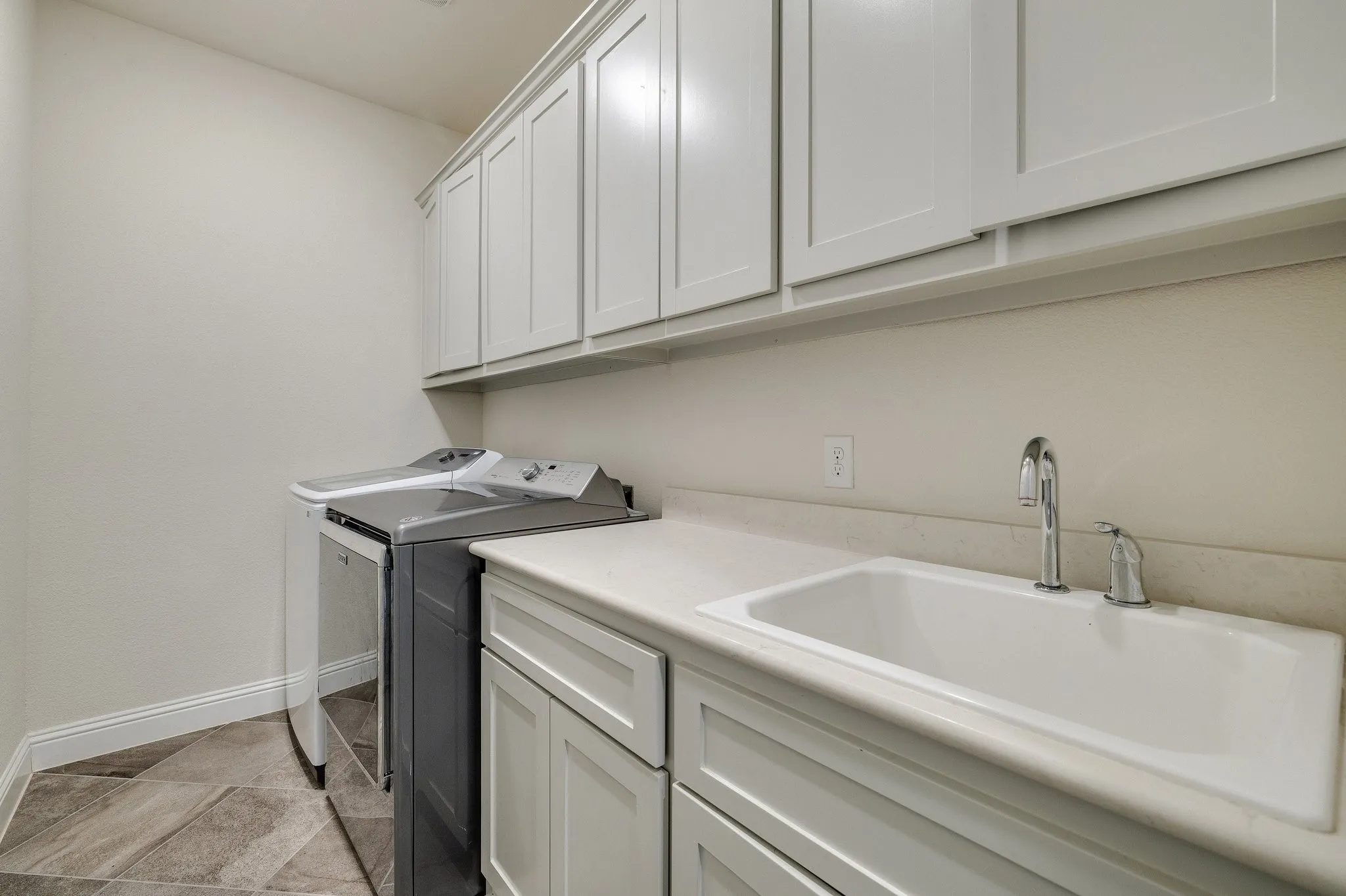 White shaker-style cabinetry, recessed lighting, white utility sink, chrome faucet, and gray-toned tile flooring