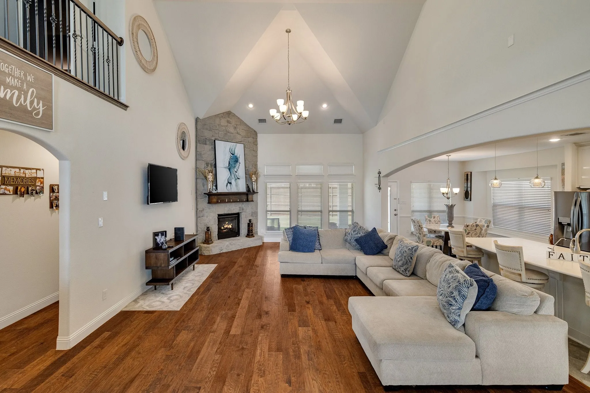 Vaulted ceiling great room with wood-finish flooring, stone-clad fireplace, and a second-story balcony featuring wrought iron spindles