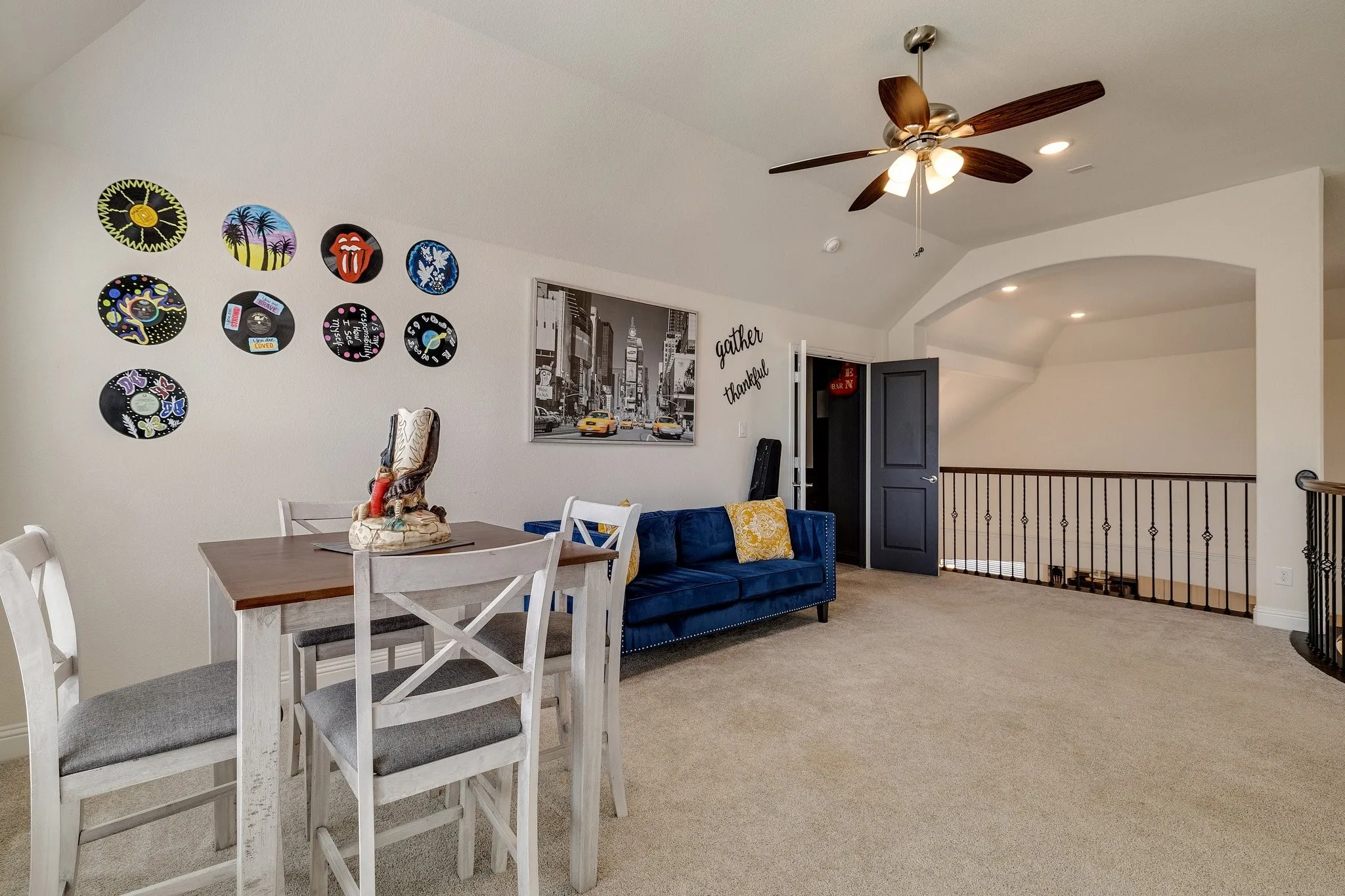 Vaulted ceiling with a ceiling fan, carpeted flooring, archway, and iron railing