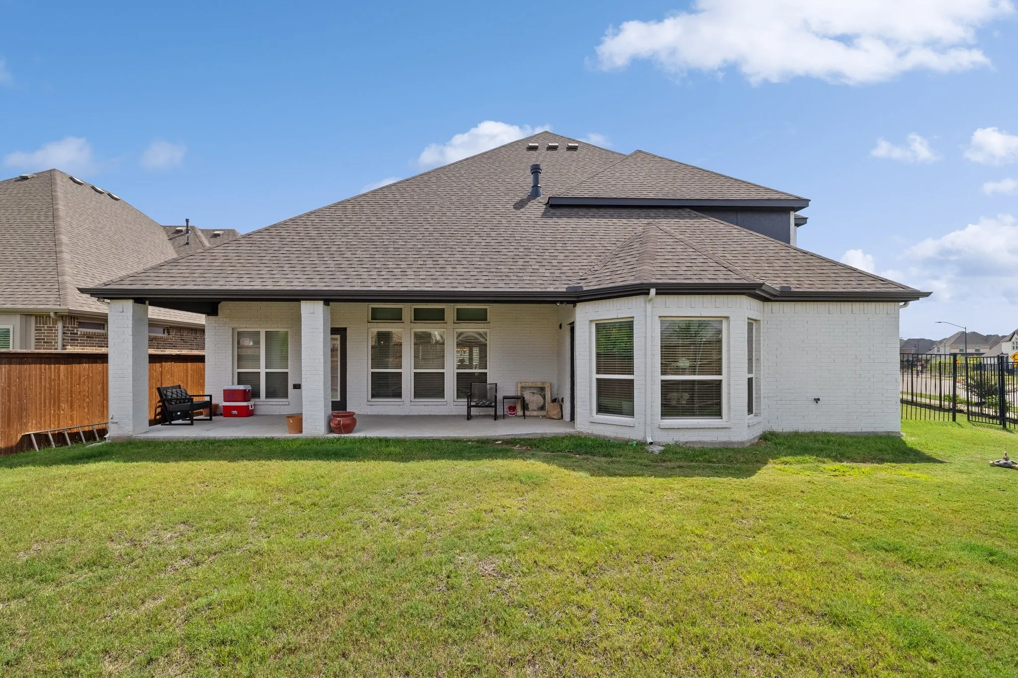 Expansive backyard with a covered patio, white brick exterior, and a bay window