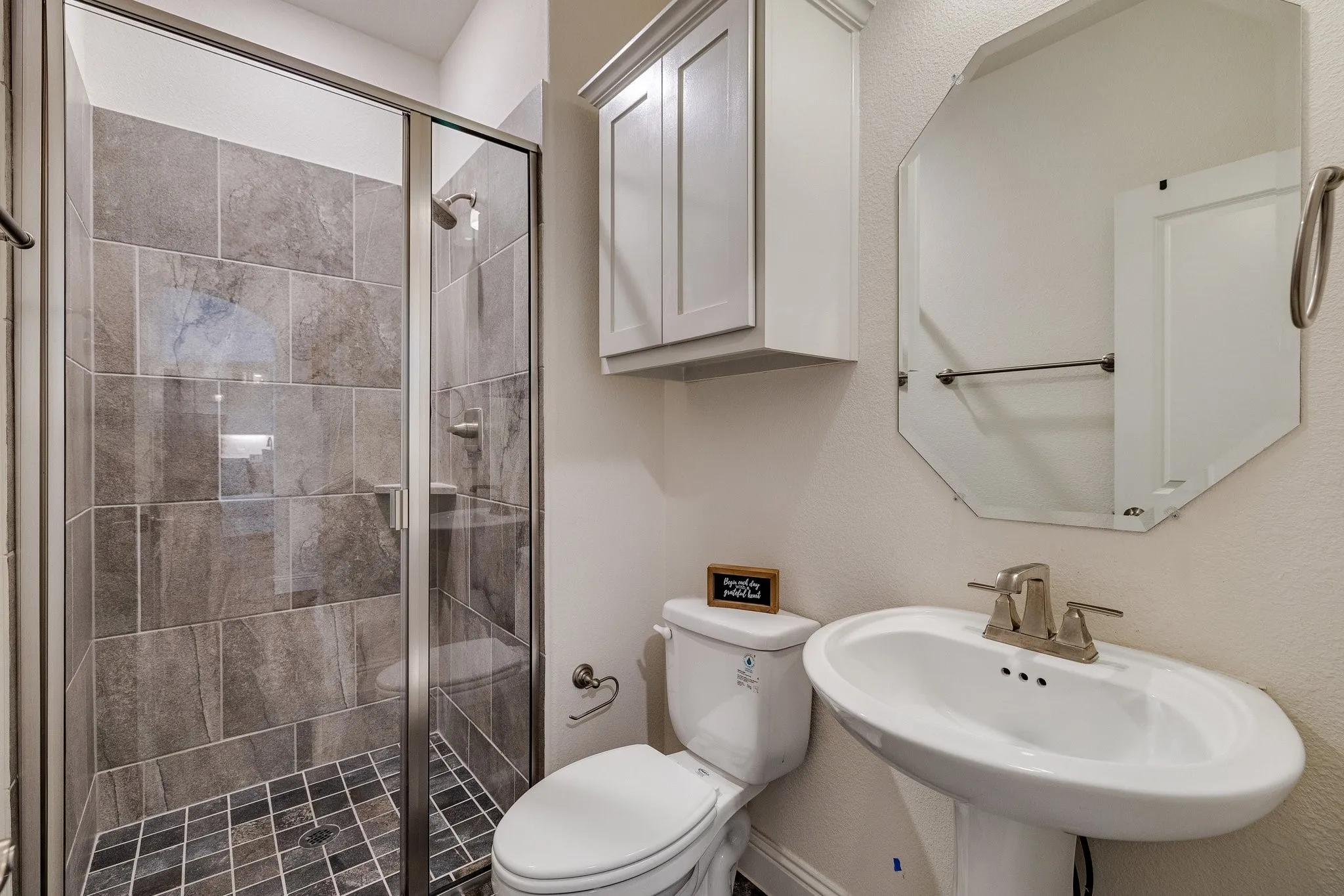 Glass-enclosed shower with gray tiled walls and dark tiled floor
