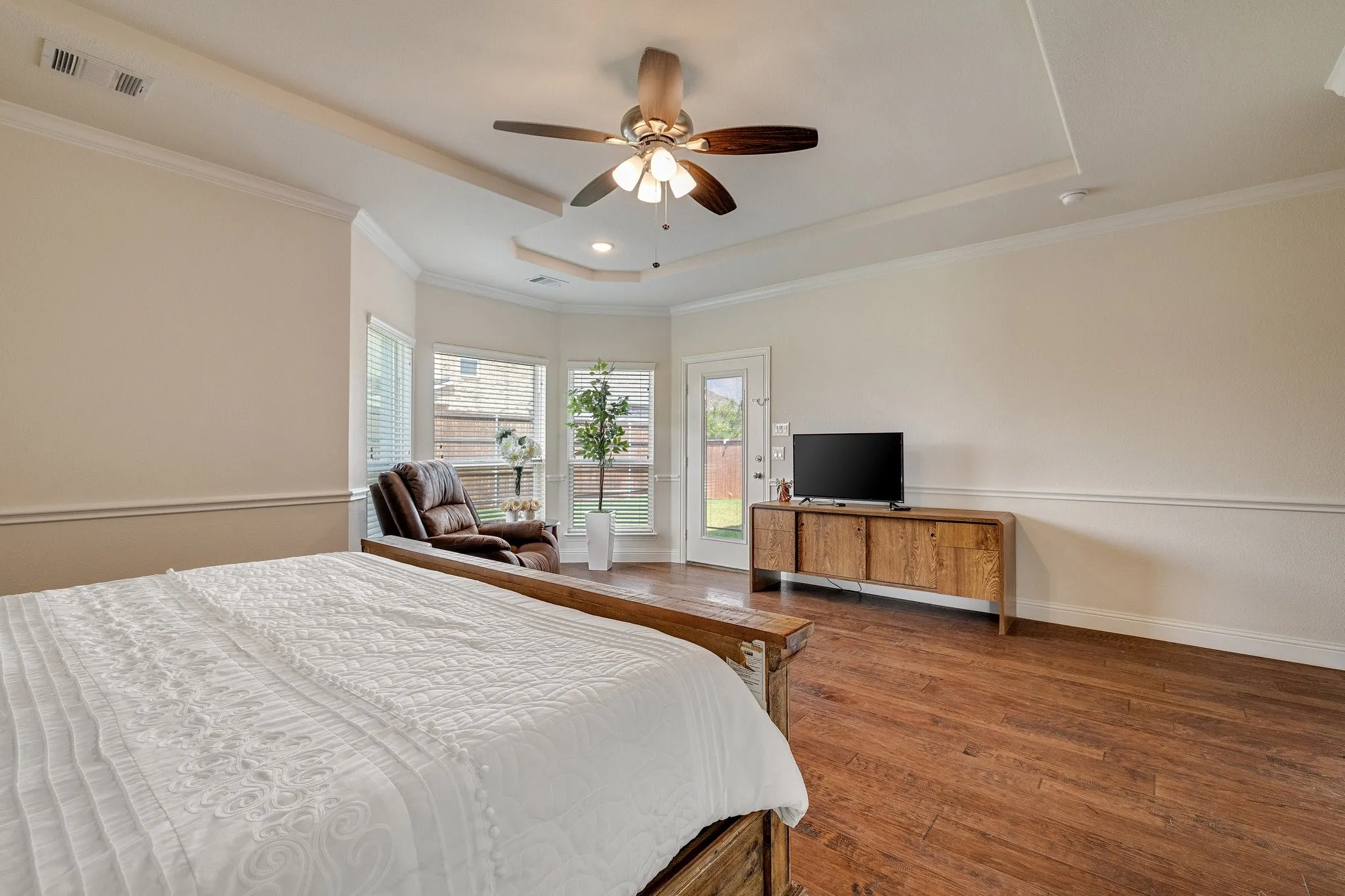 Tray ceiling with a ceiling fan, wood-finish flooring, bay window, crown molding, and direct outdoor access