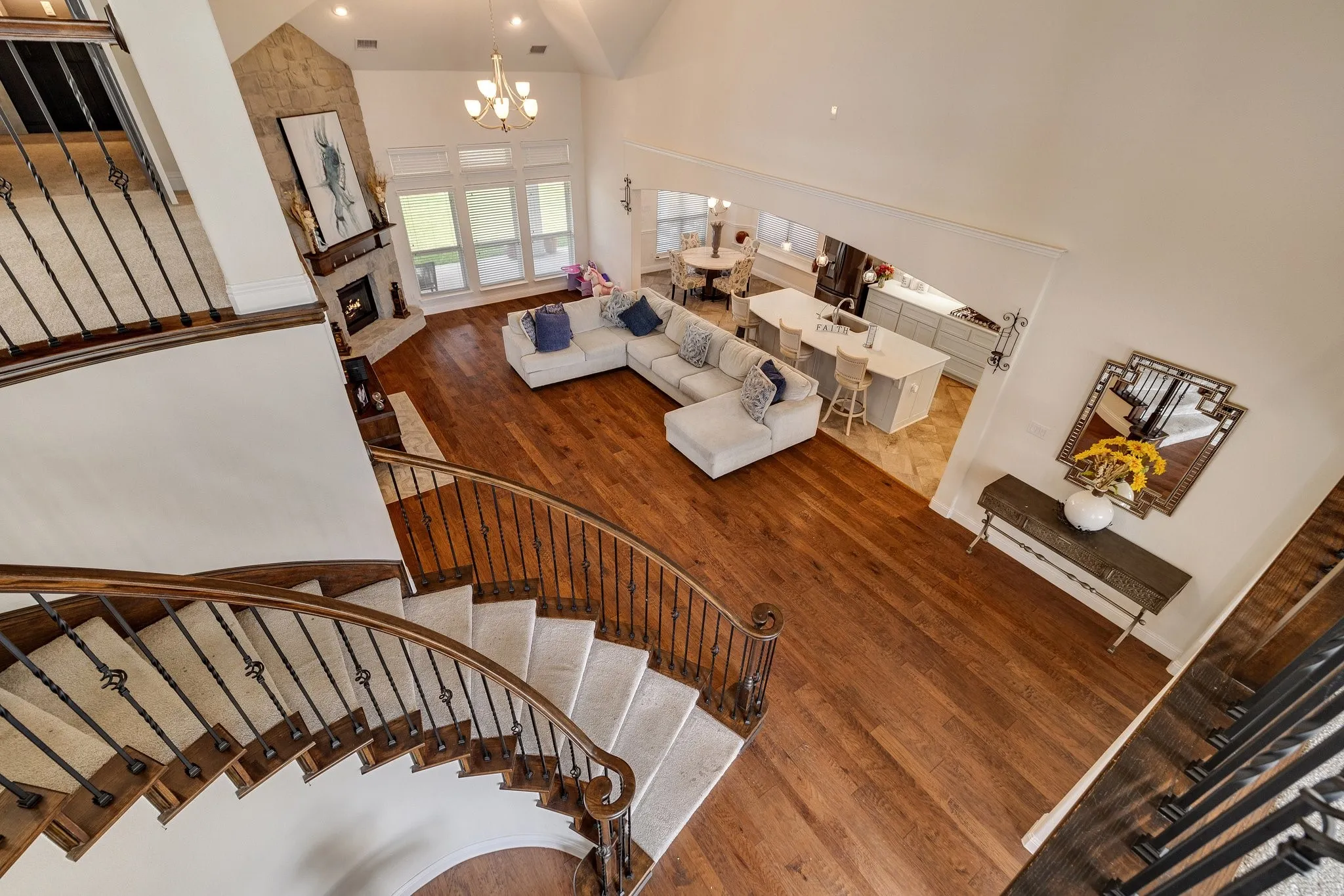 Curved staircase with wrought iron balusters, vaulted ceiling, wood-finish flooring, stone-clad fireplace, and large windows
