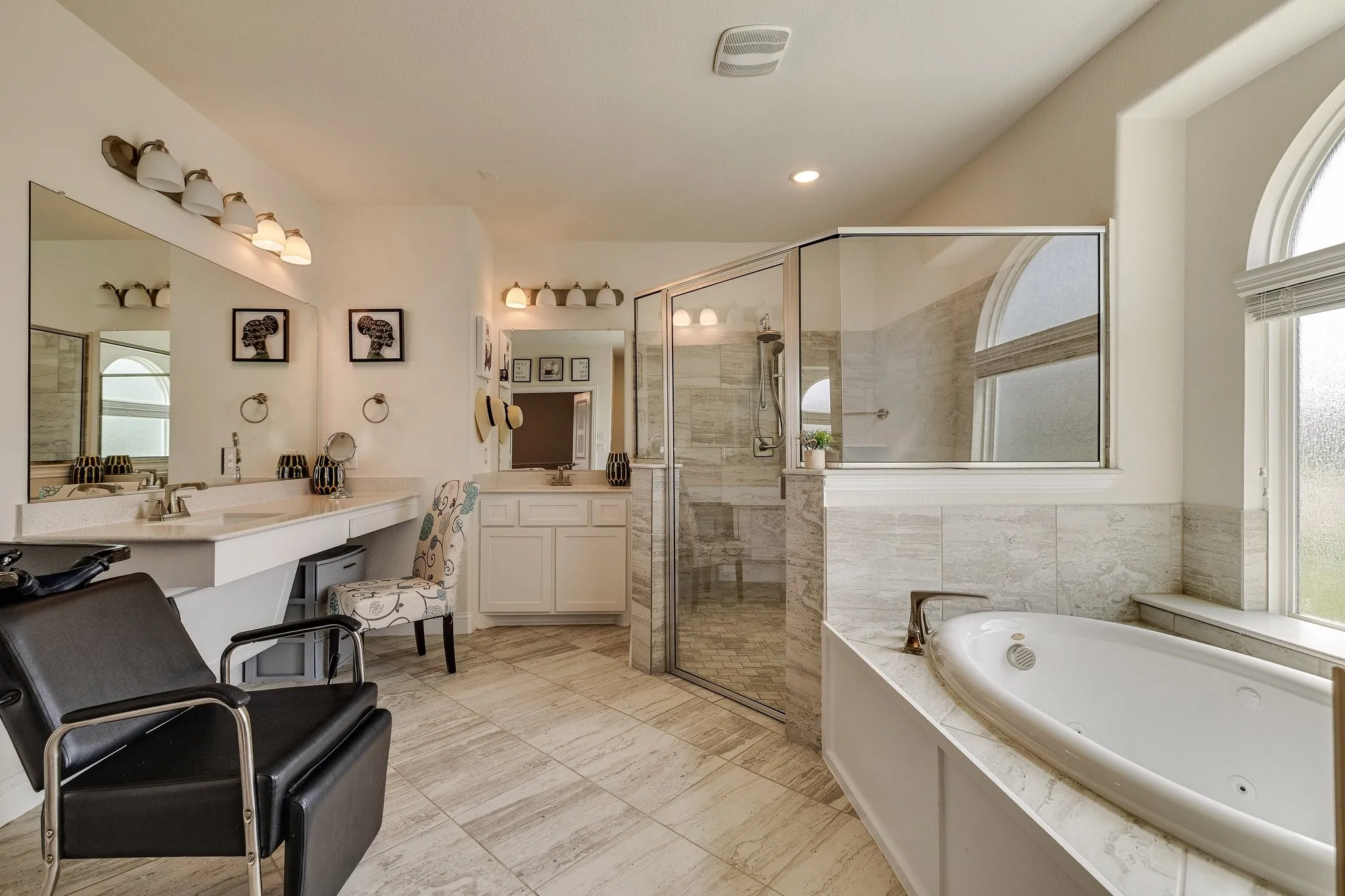 Dual vanities with integrated sinks, glass-enclosed shower, built-in jetted tub, arched windows, and tiled flooring