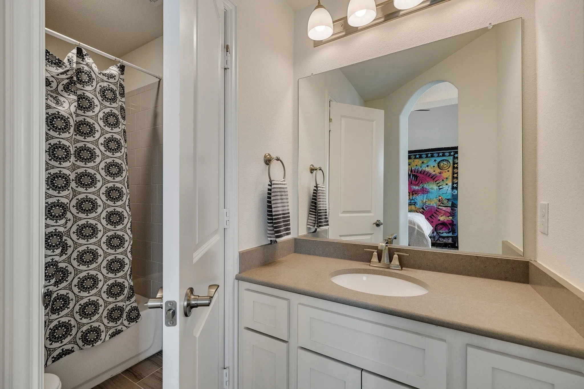 Tub-shower combination, single vanity with integrated sink, stone-finish countertop, and white cabinetry