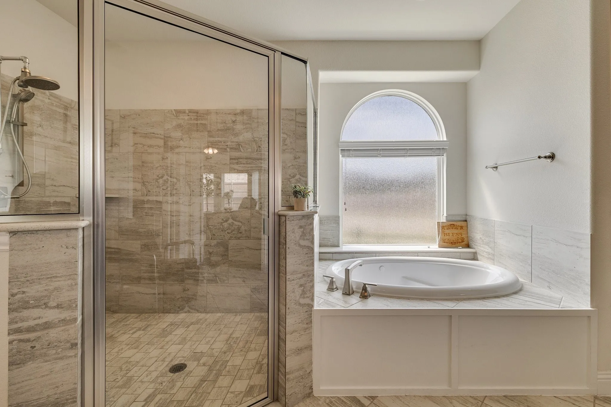 Glass-enclosed shower with a rainfall showerhead, accompanied by a built-in jetted tub featuring an arched window with frosted glass