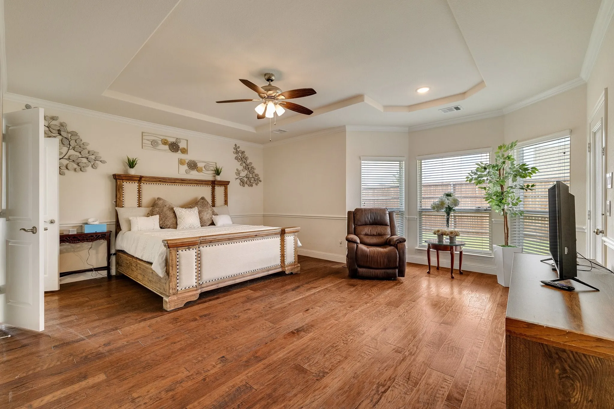 Hardwood flooring, tray ceiling, bay windows, crown molding, and a ceiling fan with integrated lighting