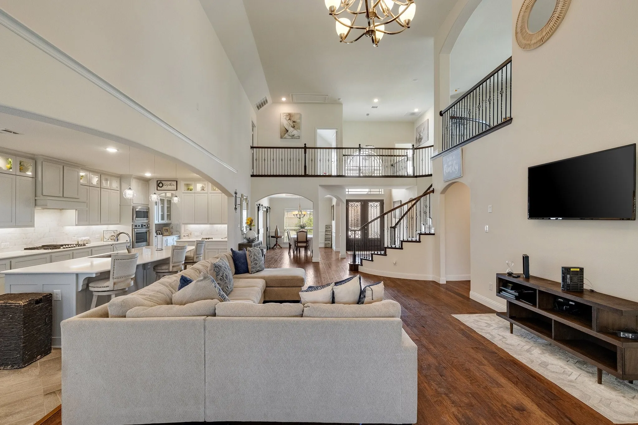Expansive open-concept living area featuring high ceilings, wood-finish flooring, and a grand staircase with wrought iron balusters