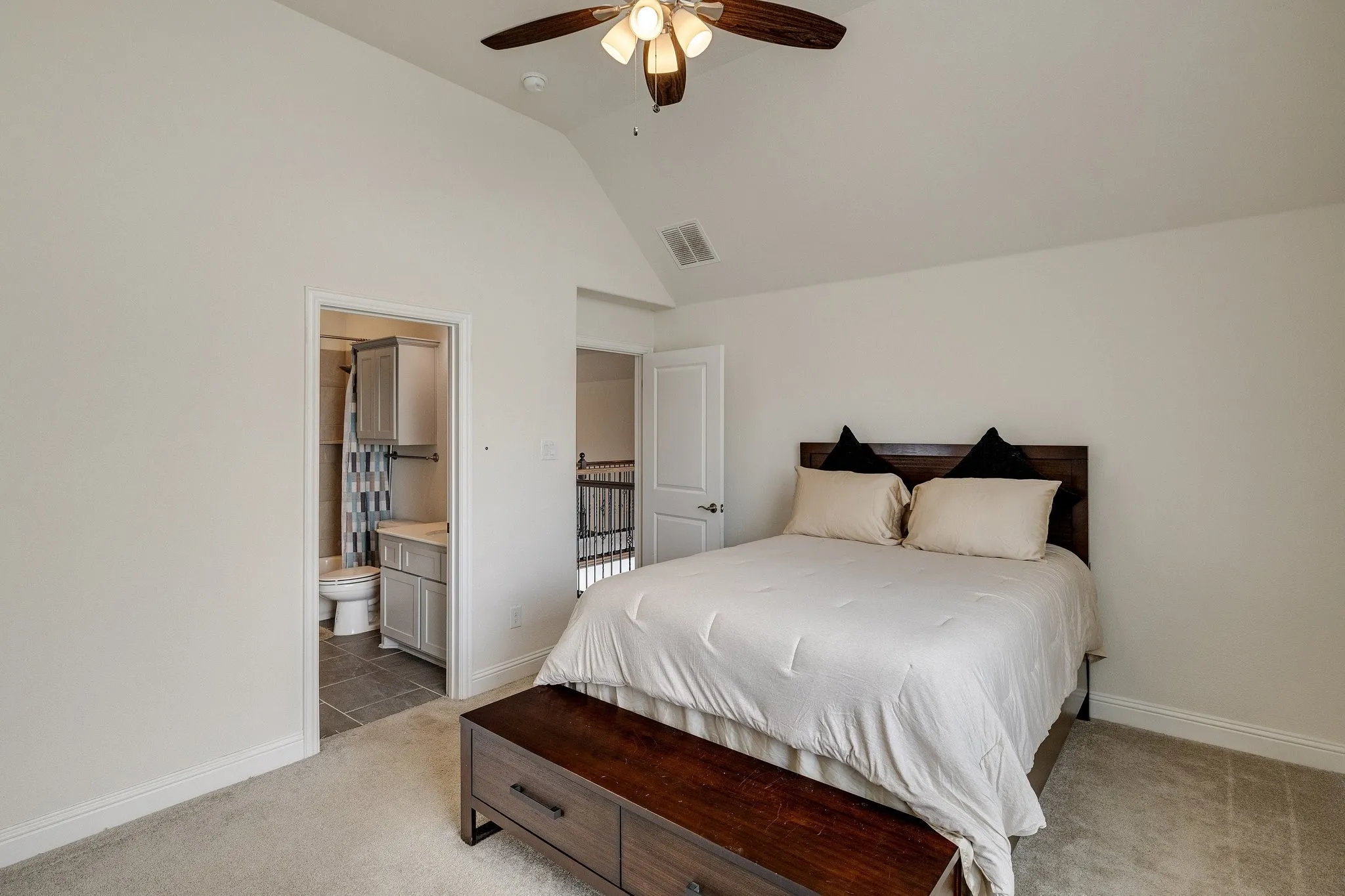 Vaulted ceiling with ceiling fan, carpeted flooring, and an en-suite bathroom featuring a vanity with under-sink cabinetry and a toilet