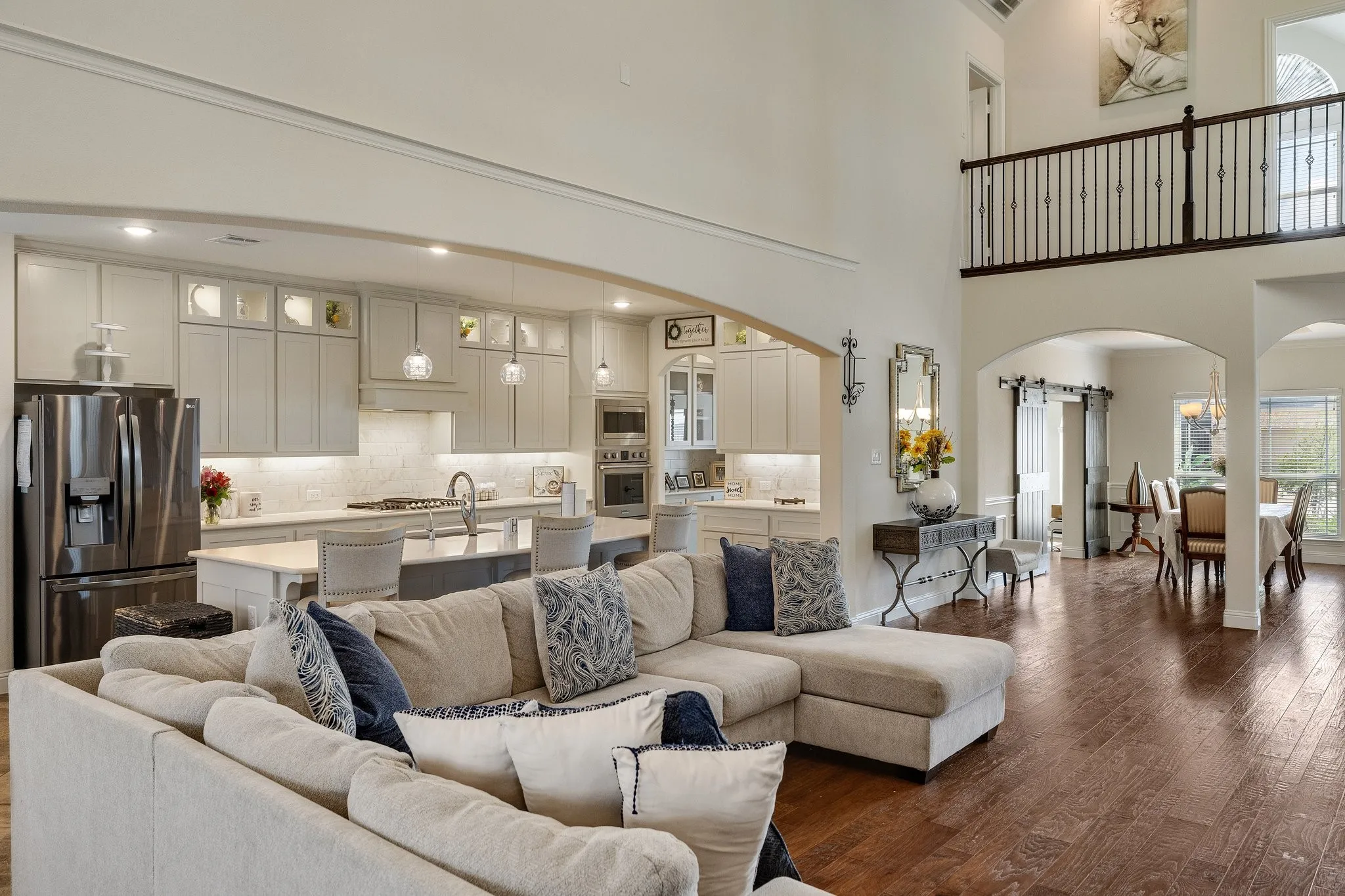 Hardwood-finish flooring, two-story ceiling, kitchen with stainless steel appliances, upper-level balcony with iron spindles, and arched doorways