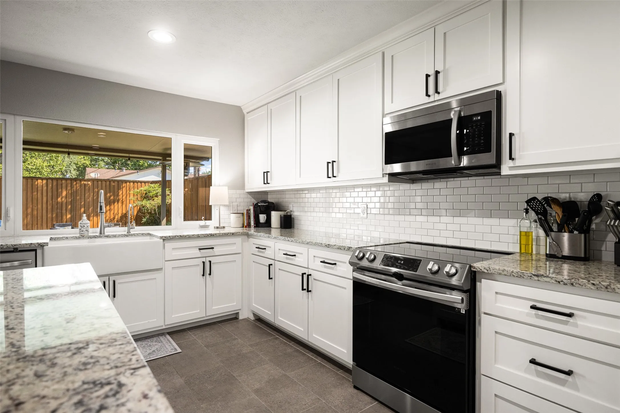 White shaker cabinetry with matte black hardware, stainless steel appliances, subway tile backsplash, light-toned stone countertops, and an undermount farmhouse sink