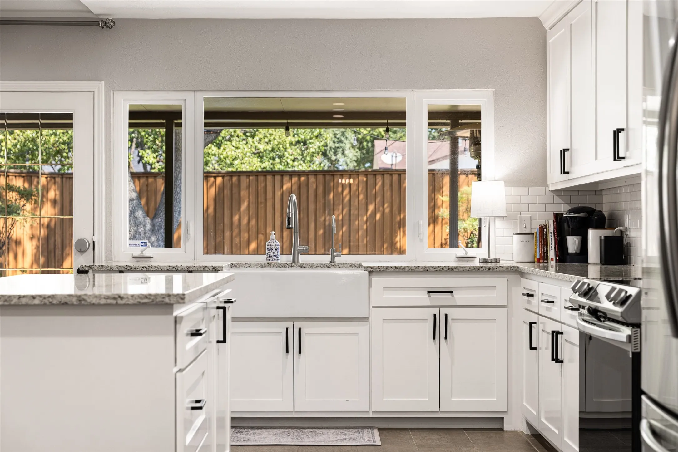 White shaker-style cabinetry with matte black hardware, stone-finish countertops, stainless steel appliances, and a farmhouse sink