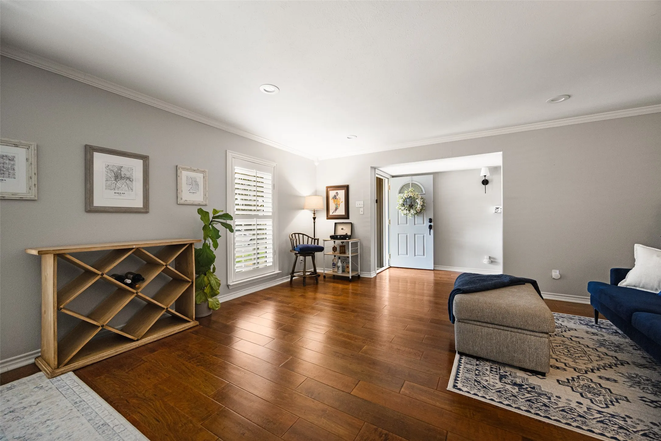 Hardwood-style flooring throughout, light gray wall paint, plantation shutters, recessed ceiling lighting, and a light blue entry door