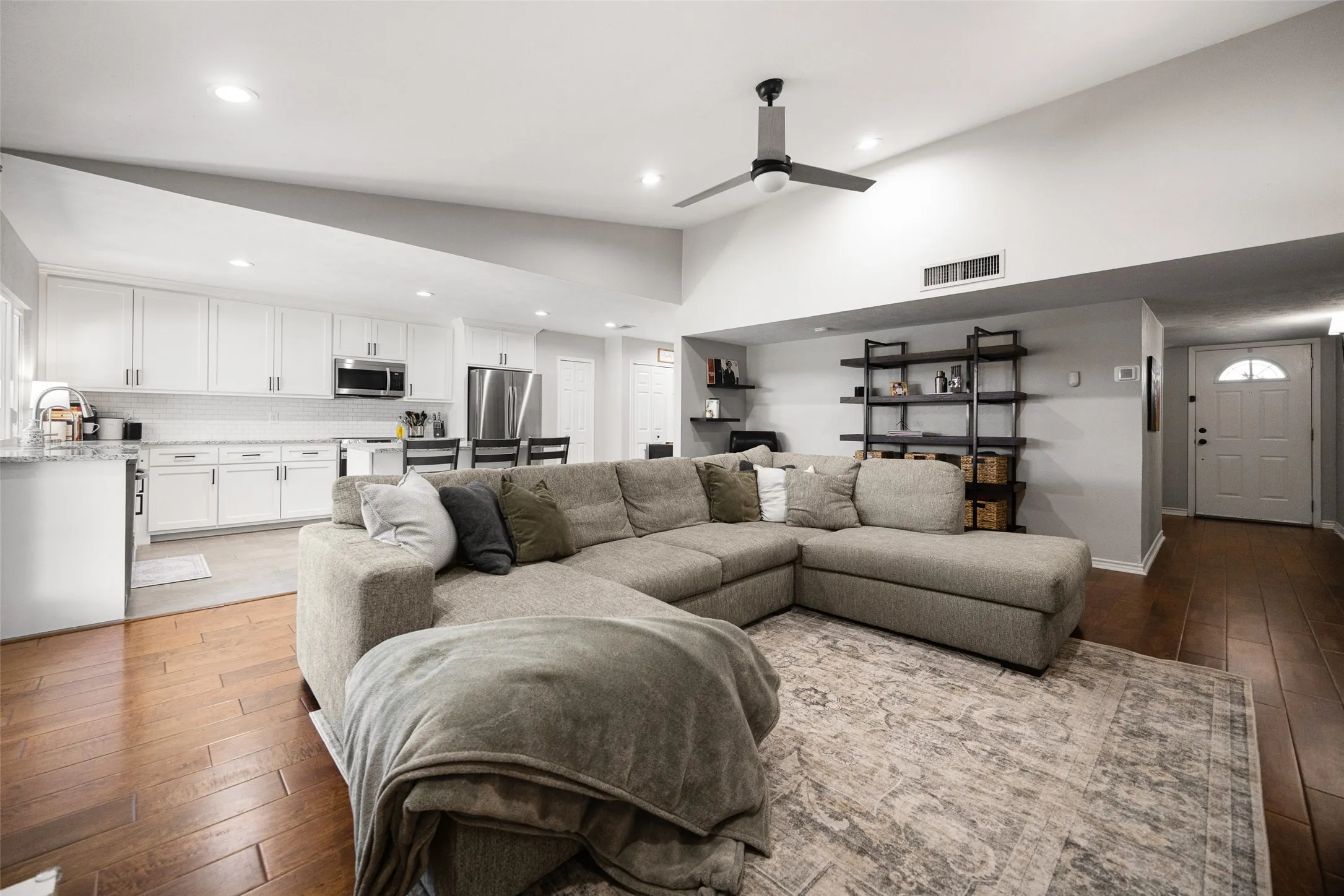 Vaulted ceiling with a ceiling fan, recessed lighting, wood-finish flooring, white cabinetry, and stainless steel appliances