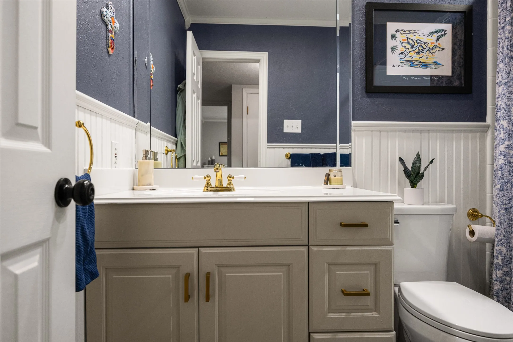Vanity with integrated sink, gold-tone fixtures, wall-mounted mirror, and beadboard wainscoting