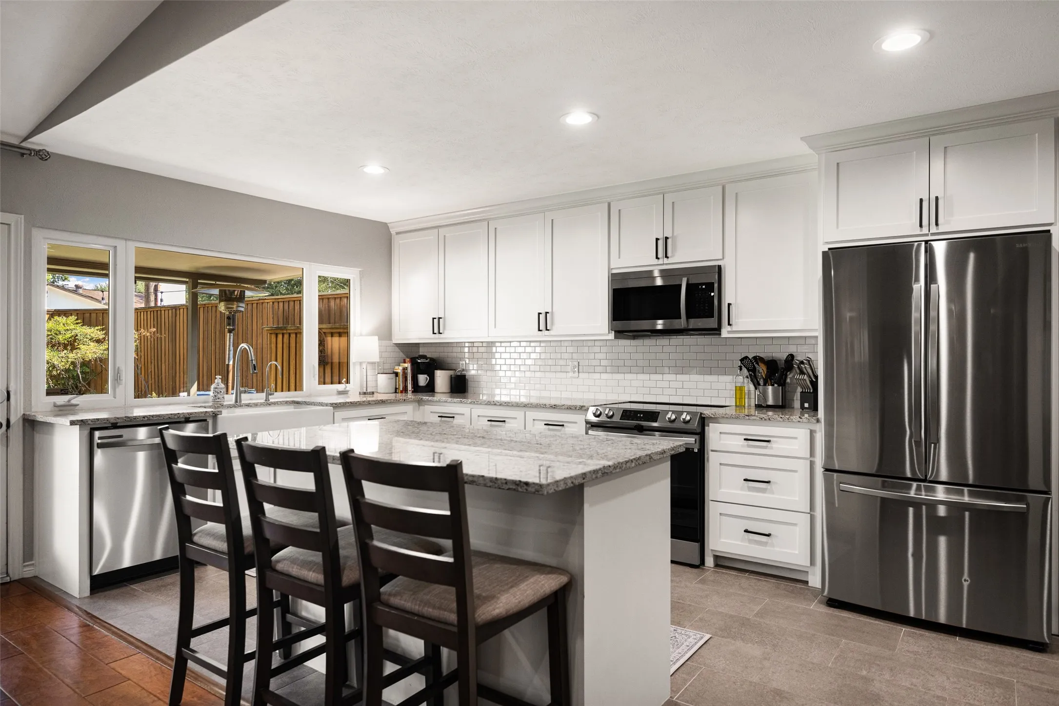 Modern kitchen featuring white shaker cabinetry, stainless steel appliances, a center island with countertop seating, and a subway tile backsplash