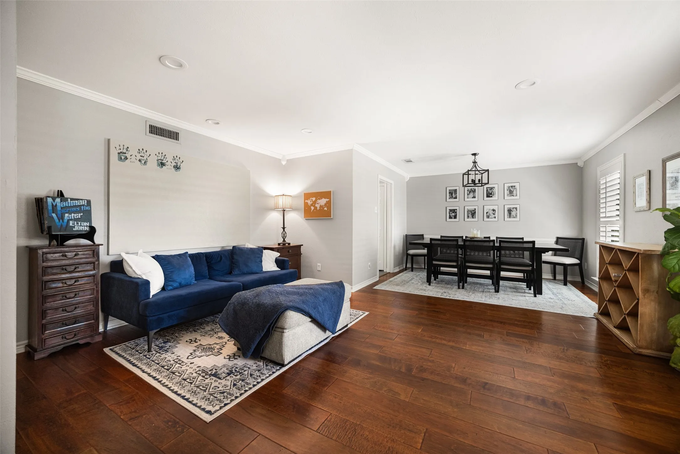 Wood-finish flooring throughout, featuring crown molding, recessed lighting, and a defined dining area with a chandelier