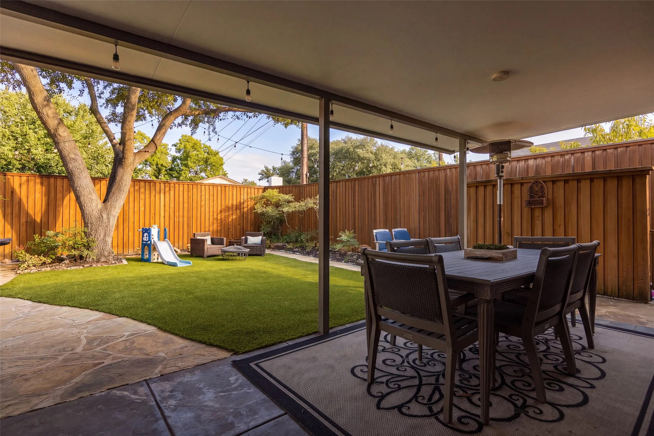 Expansive covered patio with concrete and flagstone finishes, artificial turf, and wood privacy fencing