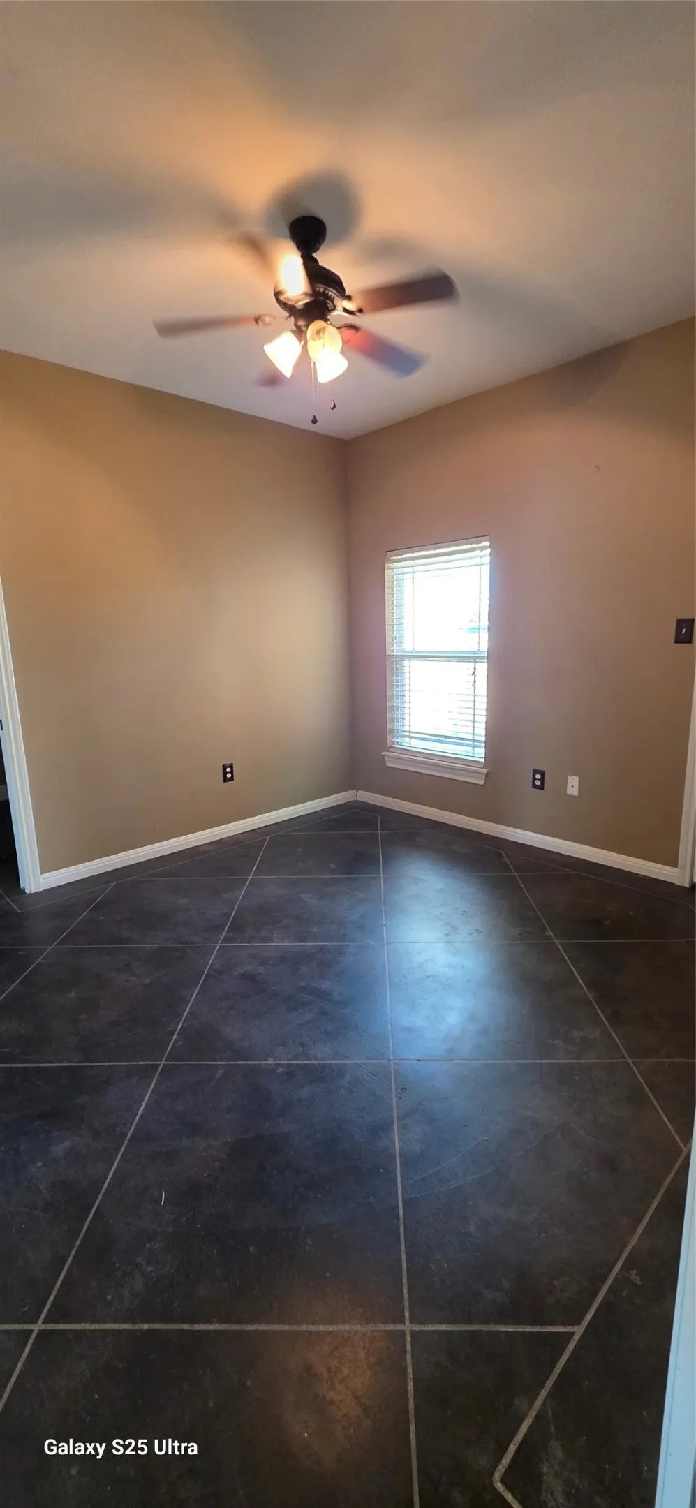 Room featuring large format floor tiles, a window with horizontal blinds, and a ceiling fan with integrated lighting