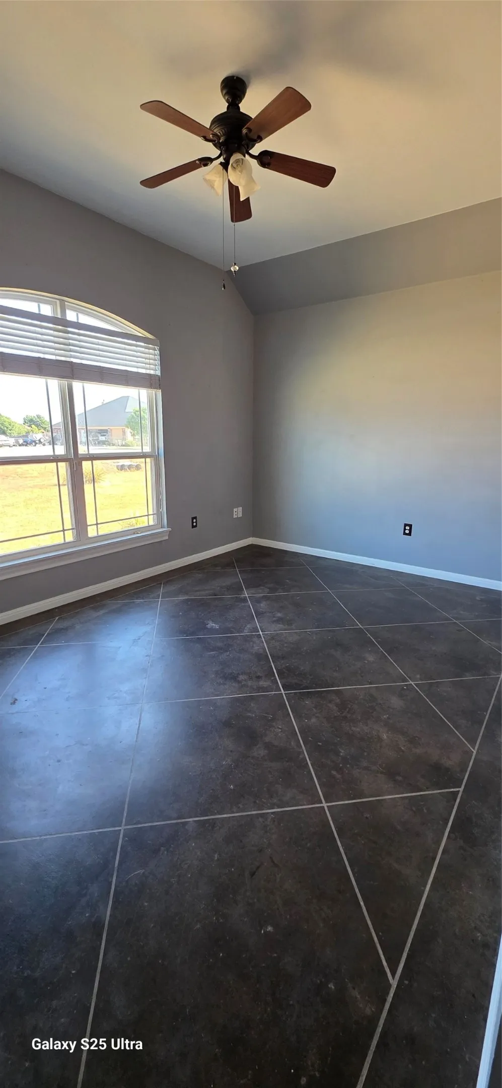Vaulted ceiling, dark tile flooring with contrasting grout, arched window with horizontal blinds, and a ceiling fan with integrated lighting