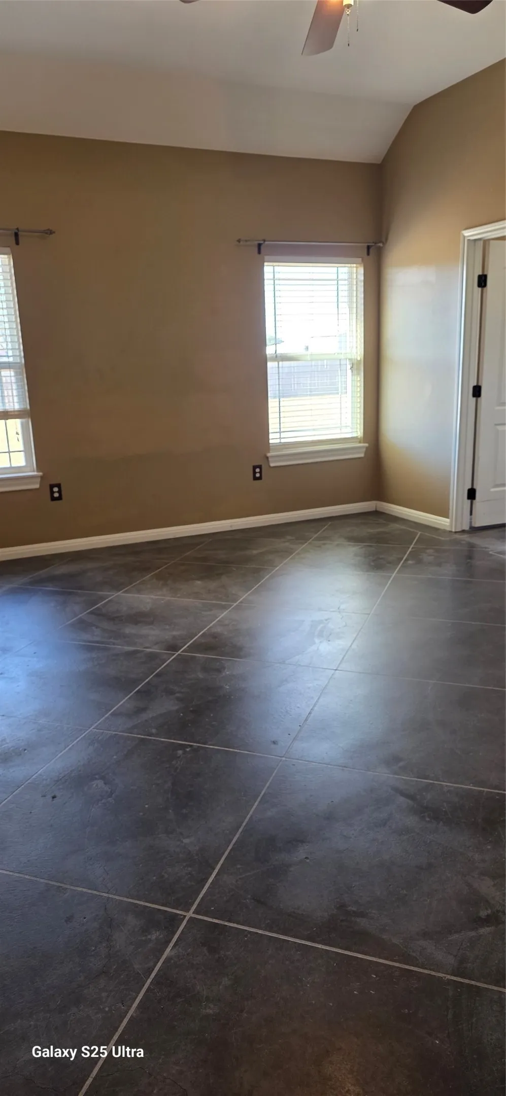 Vaulted ceiling with a ceiling fan, dual windows with blinds, and tile flooring