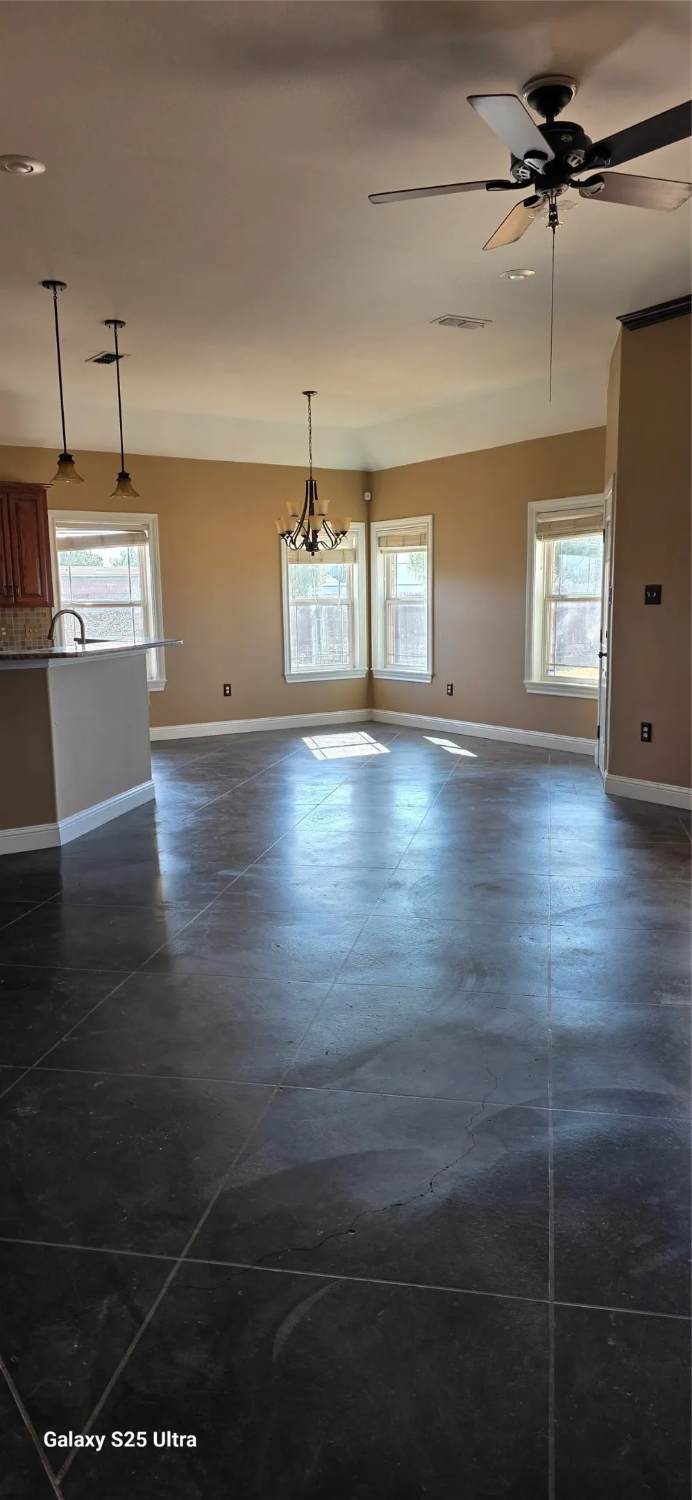 Open-concept living area featuring a large ceiling fan, dark tile flooring, and multiple windows with blinds