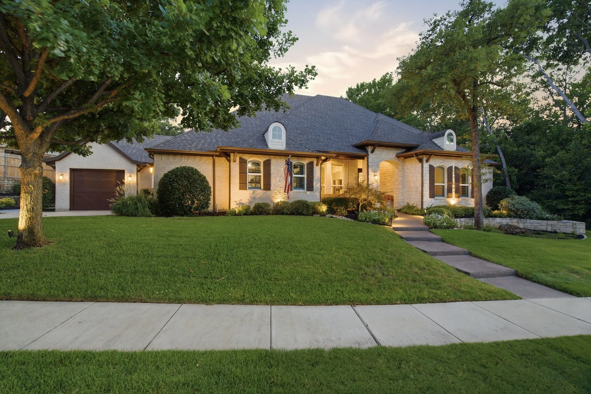 Beautiful traditional home with timeless French Country architectural influences, featuring a limestone-and-brick façade, arched details, shutters and charming dormer windows.