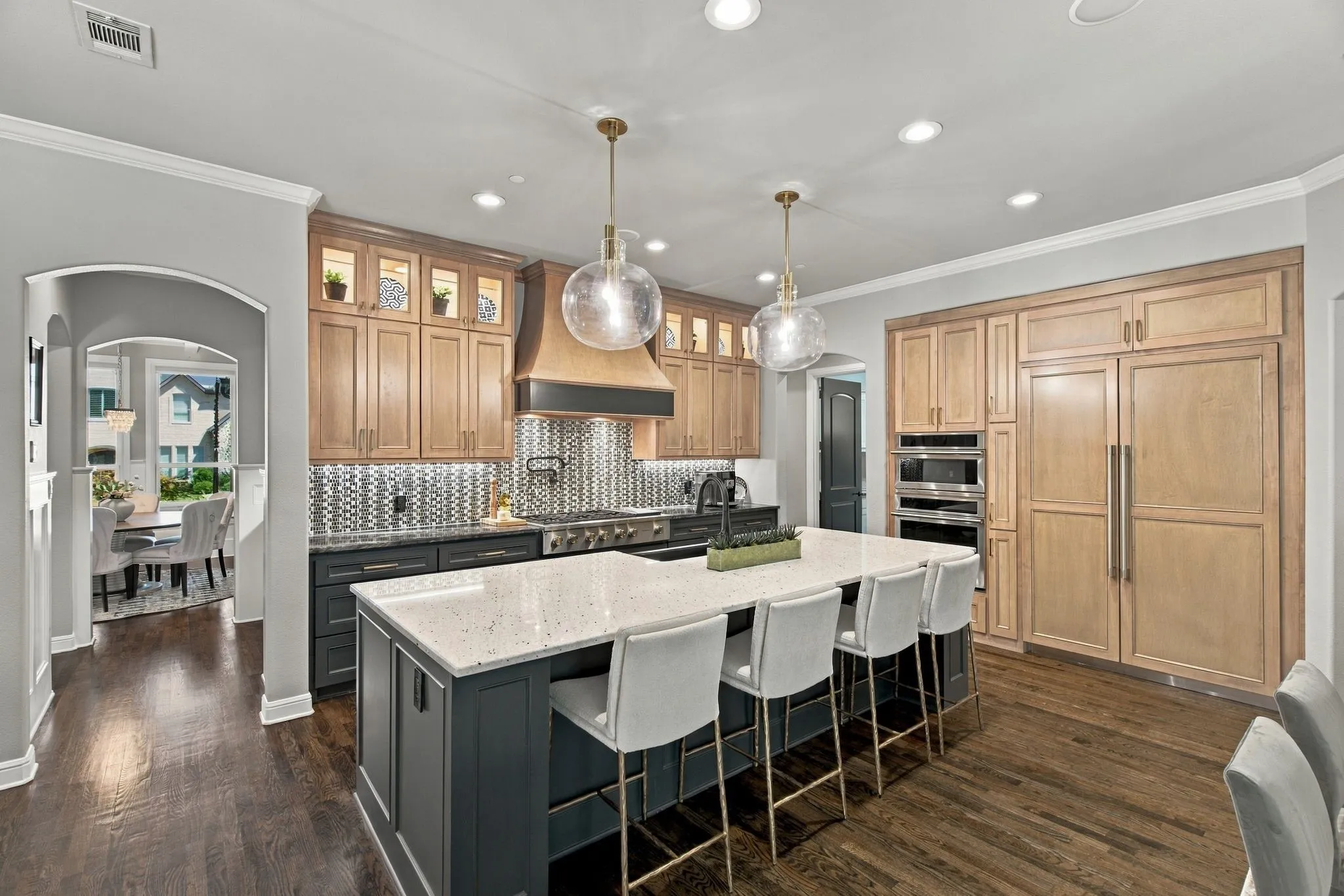 Kitchen featuring a large island with a light-toned countertop, stainless steel appliances, dark wood-finish flooring, and a mosaic tile backsplash