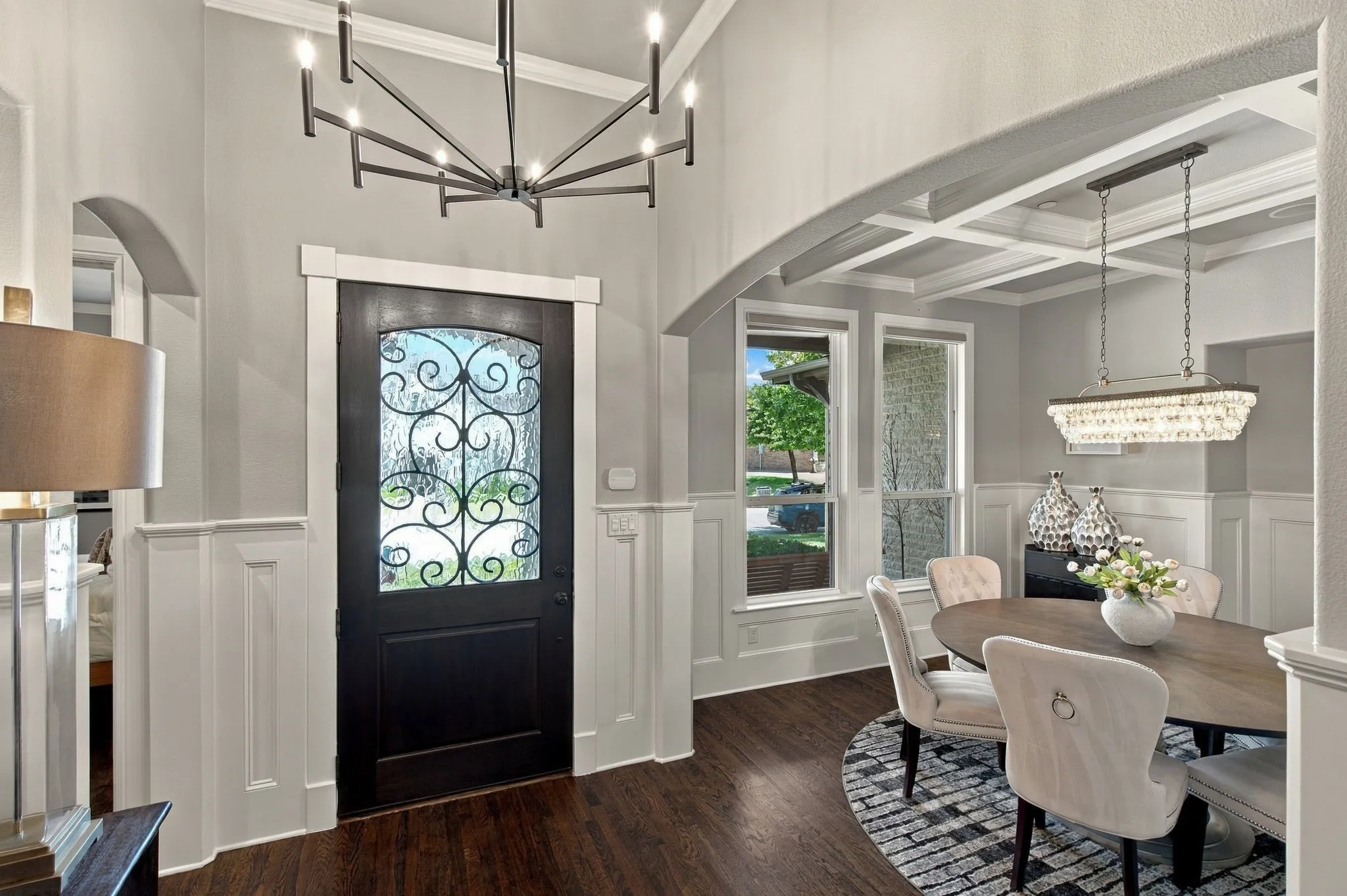 A striking entry welcomes you with rich hardwood floors and a beautiful iron-accented front door. Elegant arched openings flow into the formal dining room, where classic wainscoting, a coffered ceiling and statement lighting create a sophisticated first impression.