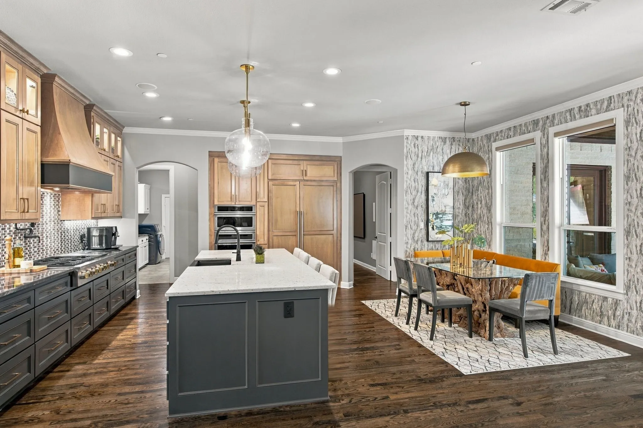 Beautifully appointed kitchen featuring an oversized center island, abundant custom cabinetry, expansive counter space and professional-style cooking amenities. Rich hardwood floors flow into the adjoining breakfast area, where large windows provide abundant natural light and views toward the outdoor living space. Designer lighting and distinctive finishes give this everyday gathering space a polished, sophisticated feel.