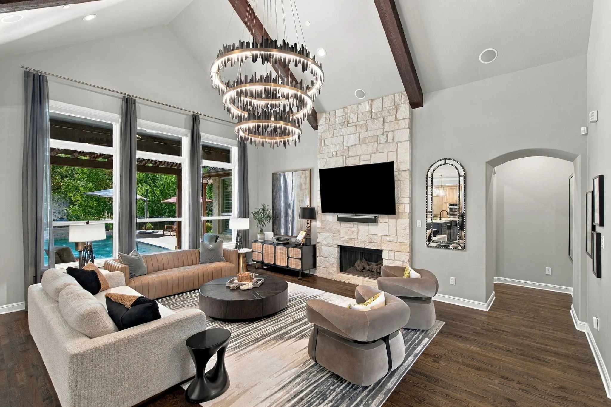 Designed to impress, the main living room pairs soaring vaulted ceilings and dramatic wood beams with a floor-to-ceiling stone fireplace and striking statement chandelier. A wall of expansive windows fills the room with natural light while creating a beautiful connection to the pool and outdoor living beyond. Rich hardwood floors add warmth to this sophisticated yet comfortable gathering space at the heart of the home.