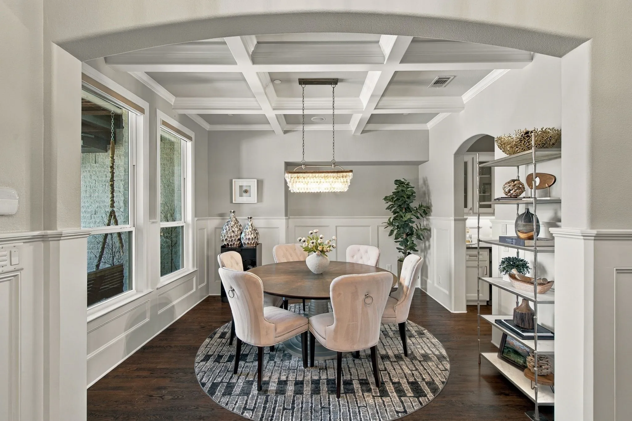 Elegant formal dining room featuring rich hardwood floors, classic wainscoting and a beautifully detailed coffered ceiling. An arched entry, abundant natural light and a statement chandelier create a sophisticated yet inviting space for both intimate dinners and special gatherings.