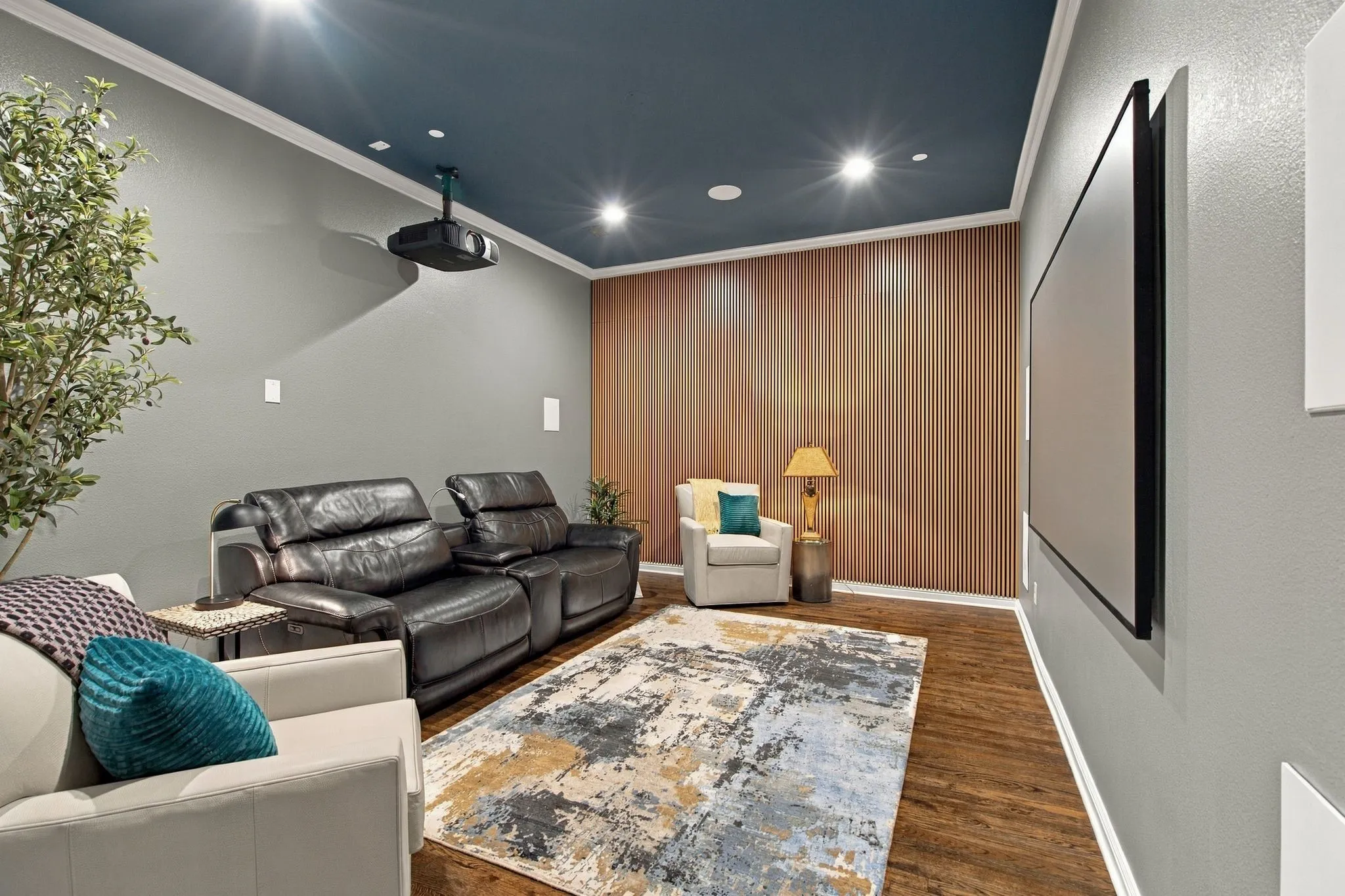 Movie night is ready! This dedicated media room creates the perfect setting for movies, sports and streaming, complete with a ceiling-mounted projector, oversized viewing screen and built-in speakers. A dramatic dark ceiling and warm wood accent wall enhance the theater atmosphere.