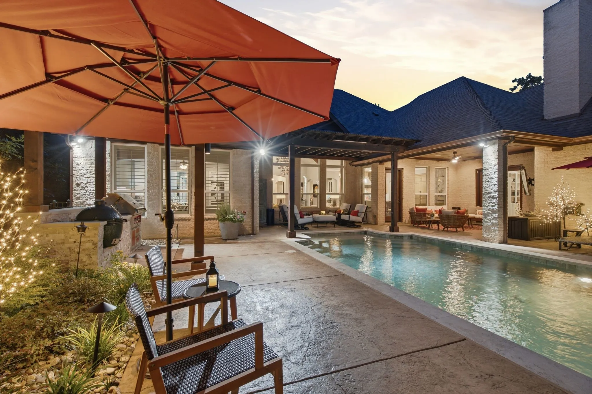Expansive outdoor living area featuring a rectangular swimming pool, stamped concrete patio, wood pergola, and an outdoor kitchen with a built-in Hestan grill and Green Egg.
