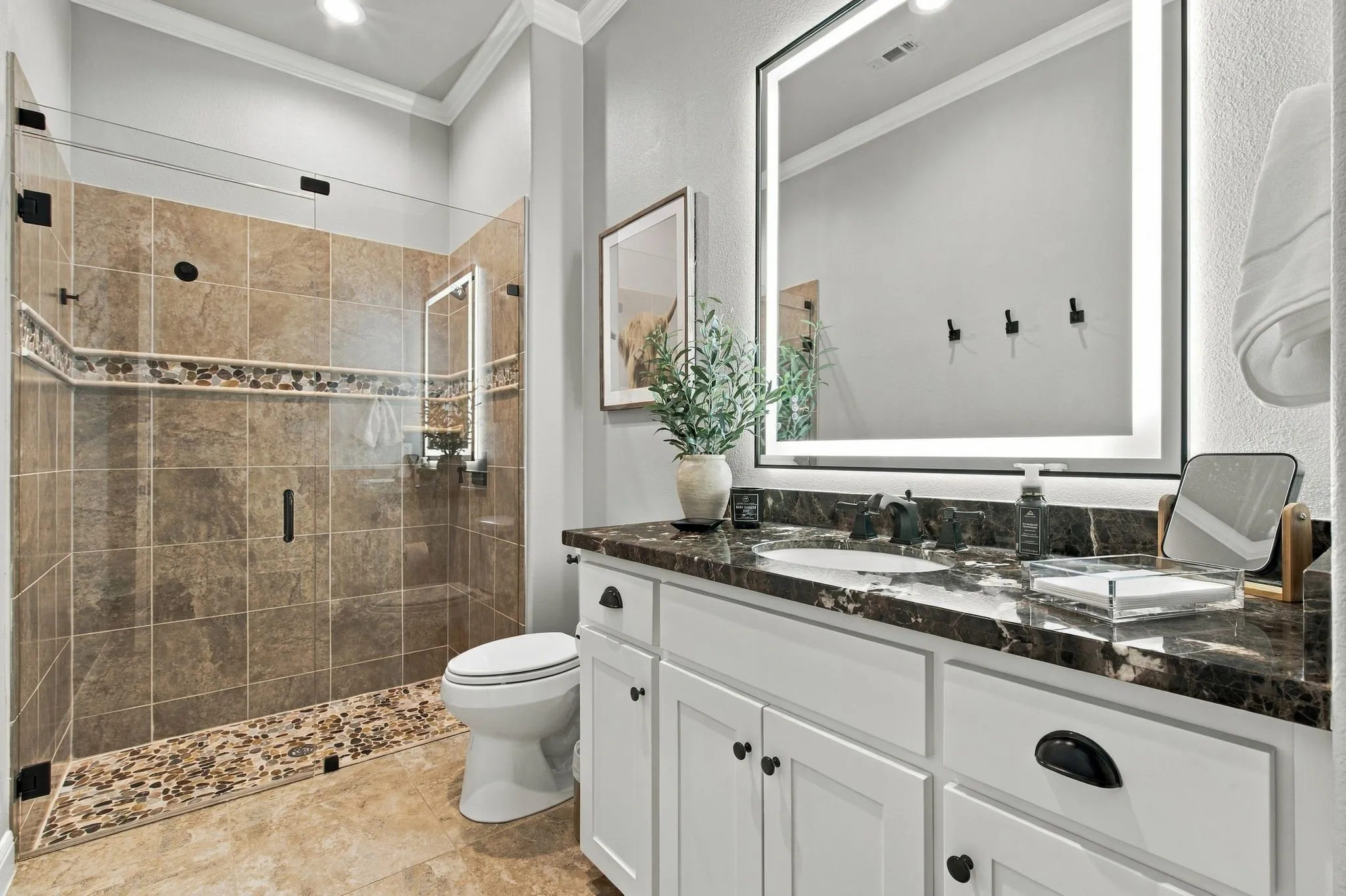 Well-appointed full bath serving the third bedroom and conveniently located near the office and media room. Features include a generous vanity with stone countertop, illuminated mirror and a spacious glass-enclosed shower with decorative tile and pebble-stone floor—combining polished style with everyday functionality.