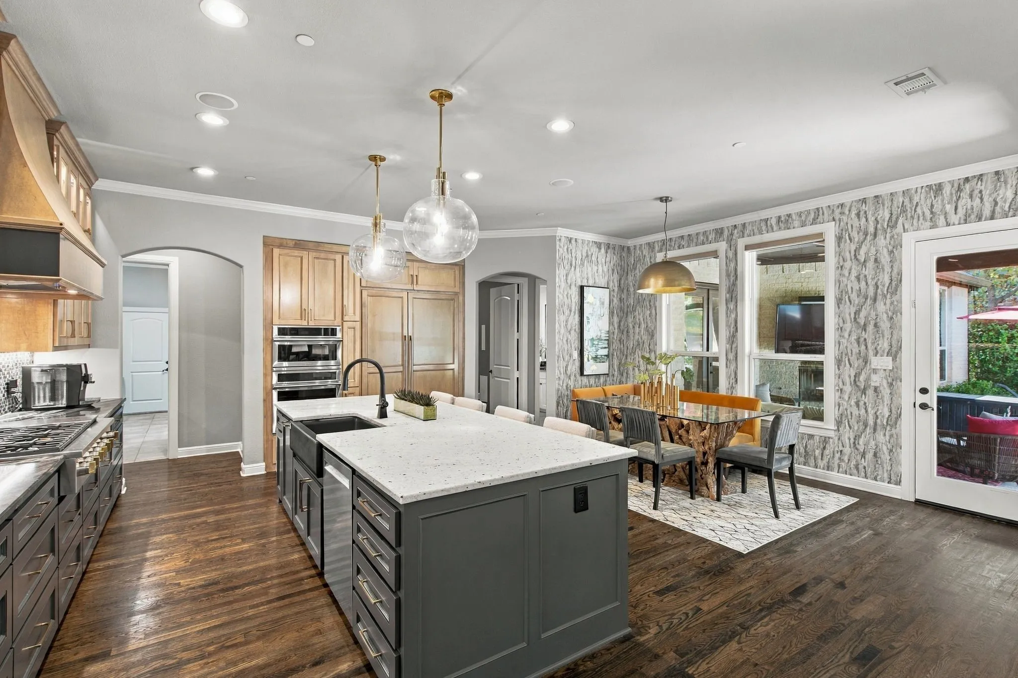 The expansive kitchen island anchors this inviting gathering space, offering generous prep space, seating and storage. Designer pendant lighting adds a polished touch, while the adjoining breakfast area is surrounded by windows and opens directly to the covered outdoor living area—creating an easy connection between indoor and outdoor entertaining.