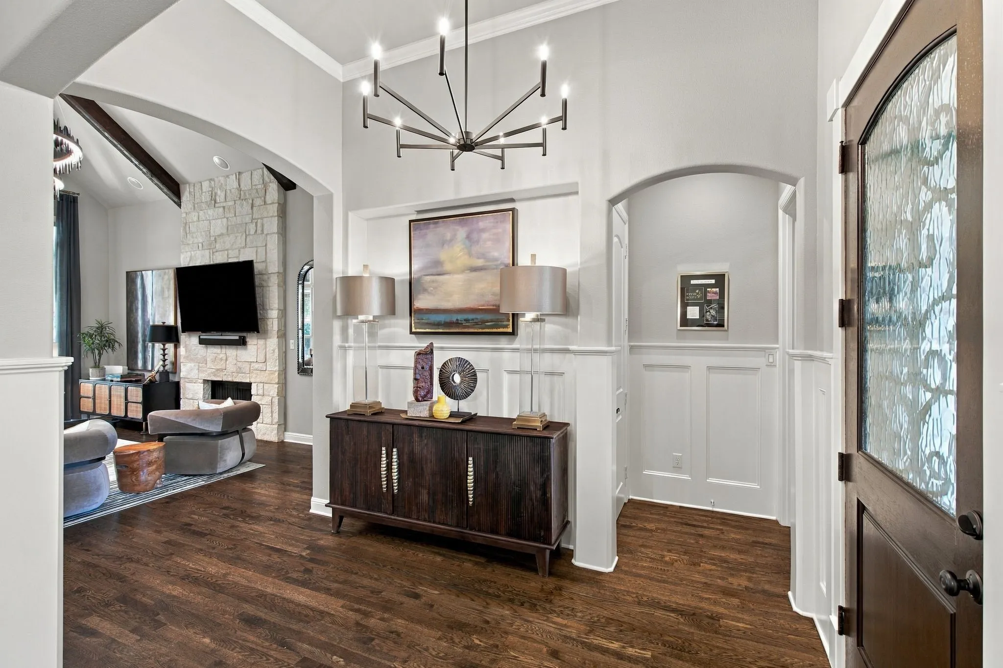 Impressive foyer featuring soaring ceilings, rich hardwood floors, classic wainscoting and graceful arched openings. A dramatic modern chandelier and decorative glass entry door add distinctive character, while the open design provides a beautiful transition into the main living areas.