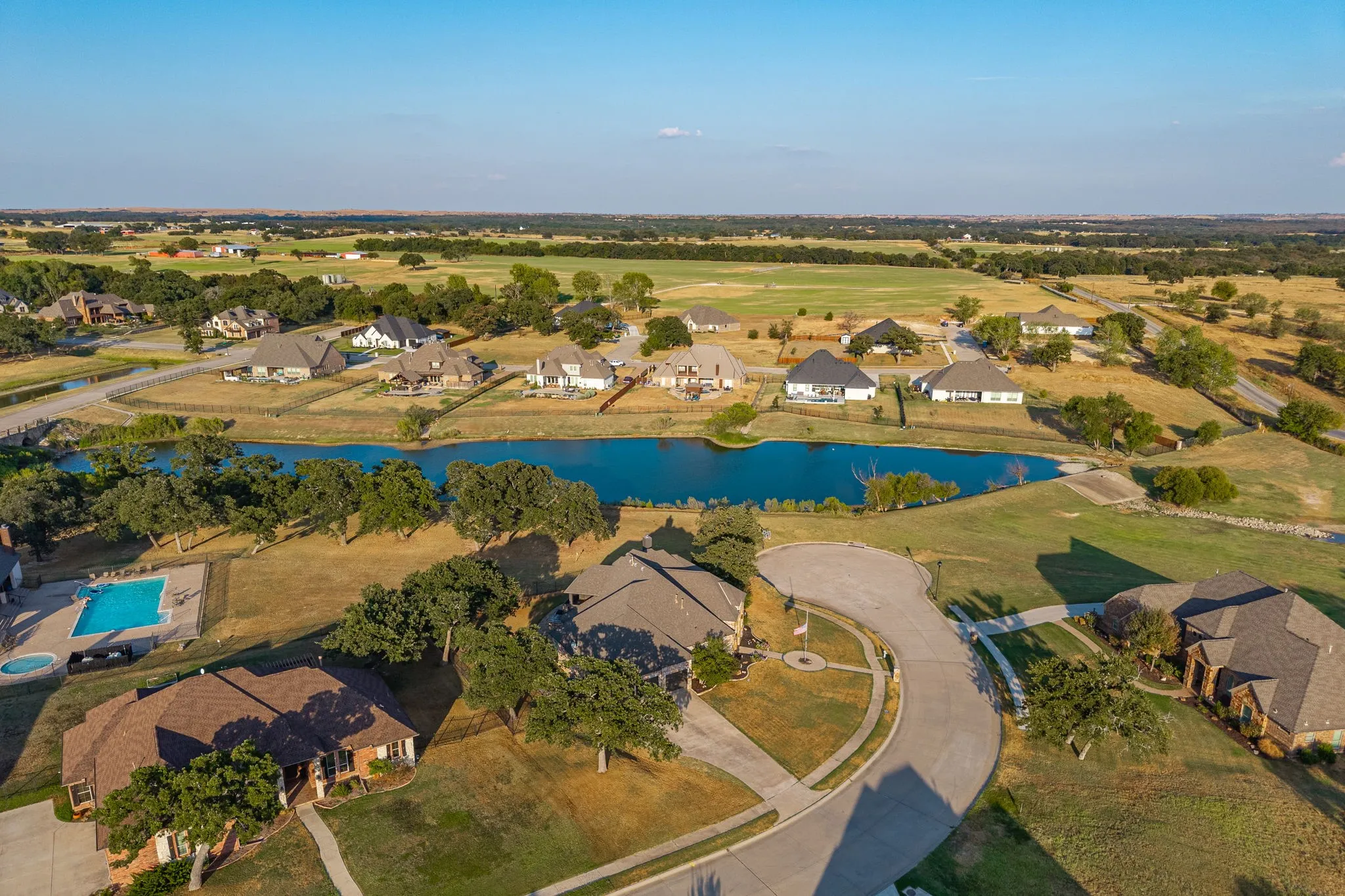 Aerial perspective showcasing a residential community with a central water feature, mature trees, and an in-ground swimming pool