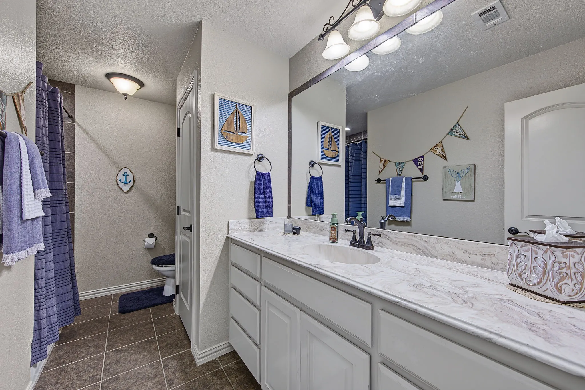 Upstairs guest full bath wit white vanity with integrated sink, expansive countertop, large mirror, and overhead vanity lighting
