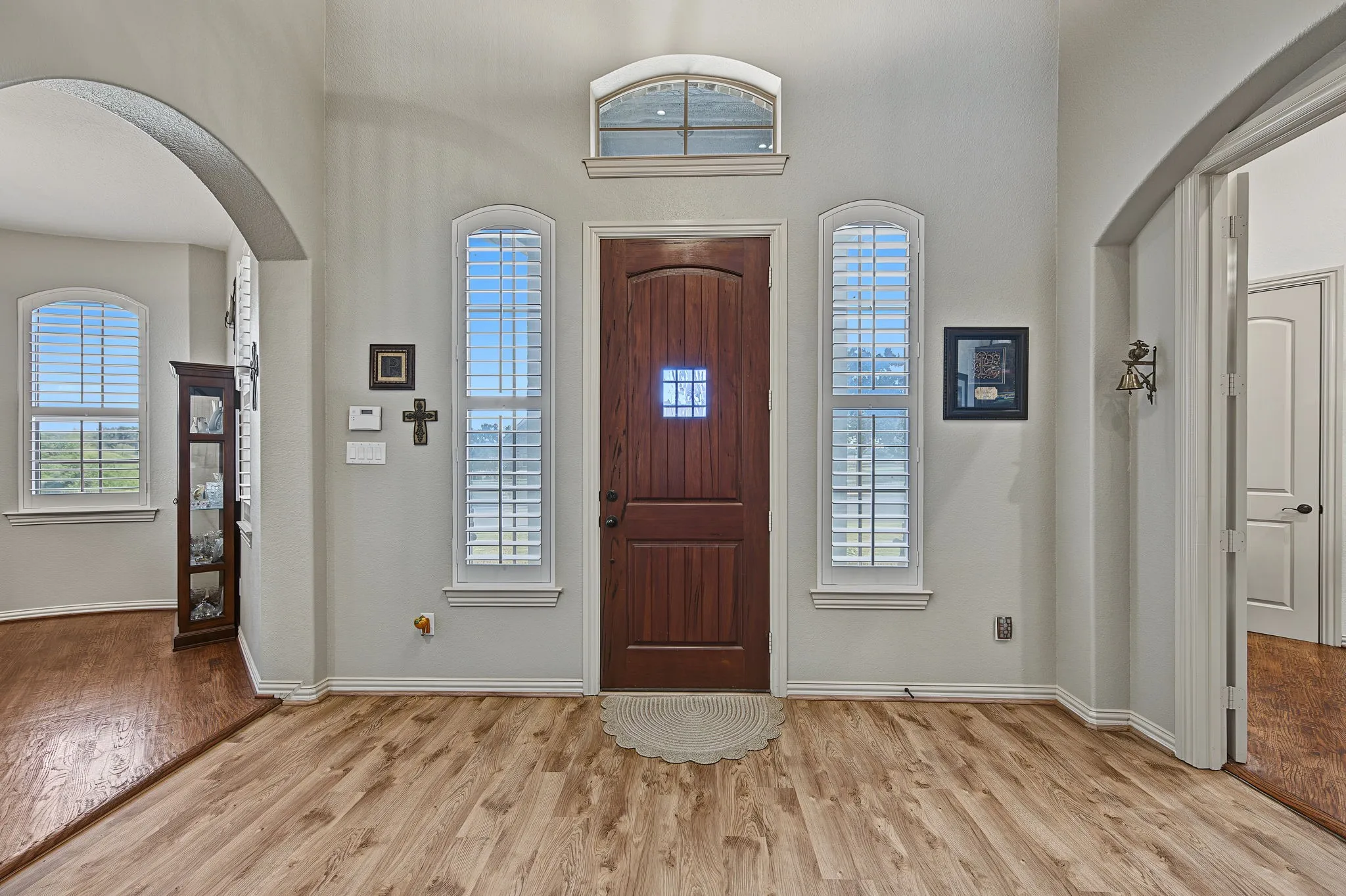 Wood-finish flooring with arched doorways, a wood-panel entry door, and tall windows with plantation shutters