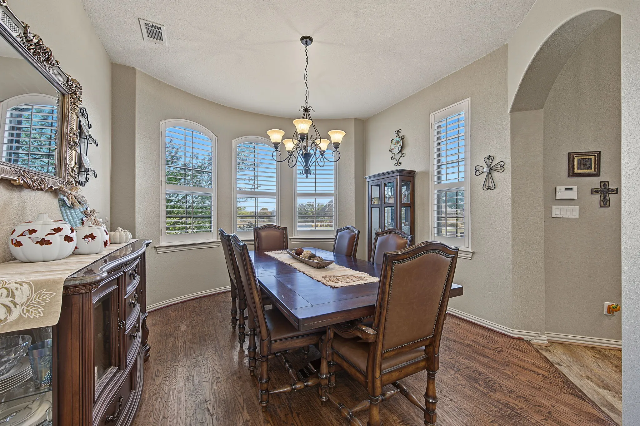 Recessed bay window with multiple arched windows, plantation shutters, wood-finish flooring, and a chandelier lighting fixture