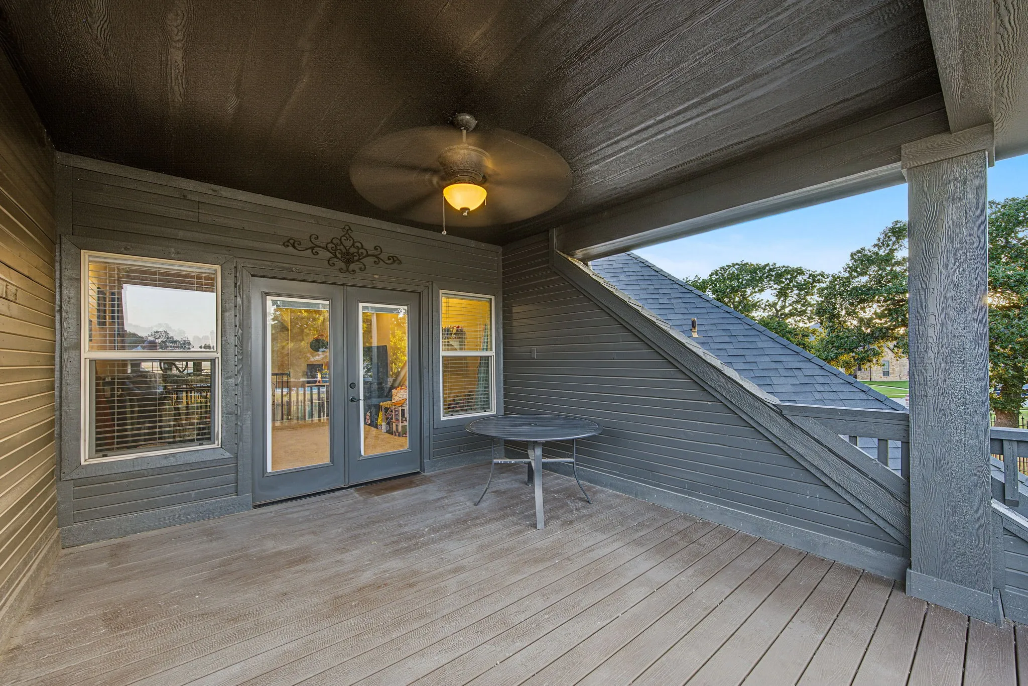 Covered outdoor deck with ceiling fan, wood-look flooring, and double glass-paneled doors