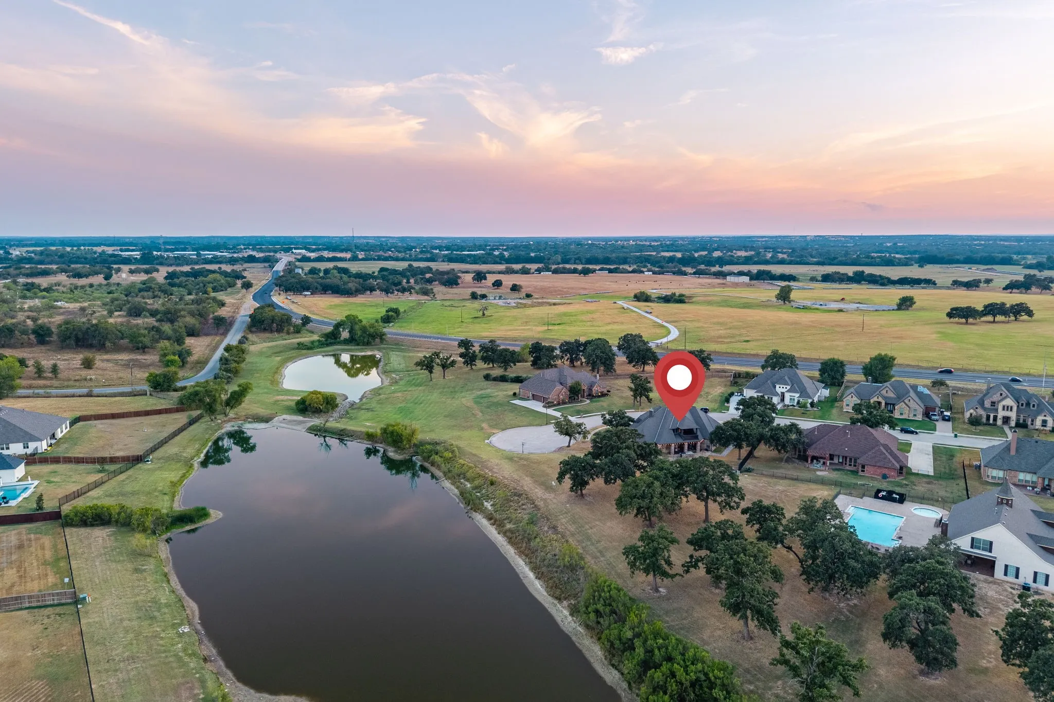 Aerial perspective showcasing the property situated among other residences, featuring a large body of water, extensive green spaces, and a paved road