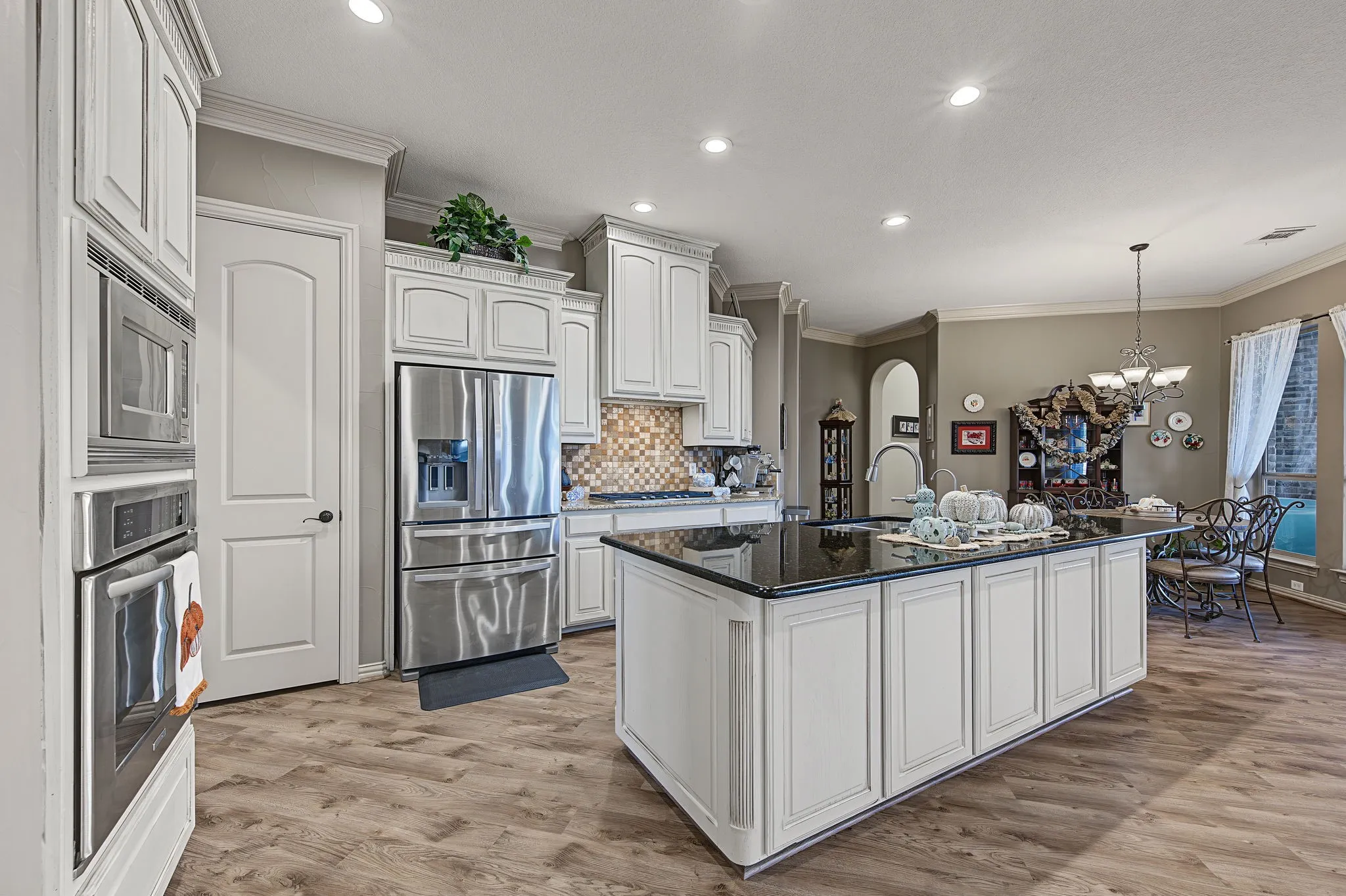 Kitchen featuring white cabinetry, stainless steel appliances, a large island with a dark countertop, wood-finish flooring, and recessed lighting