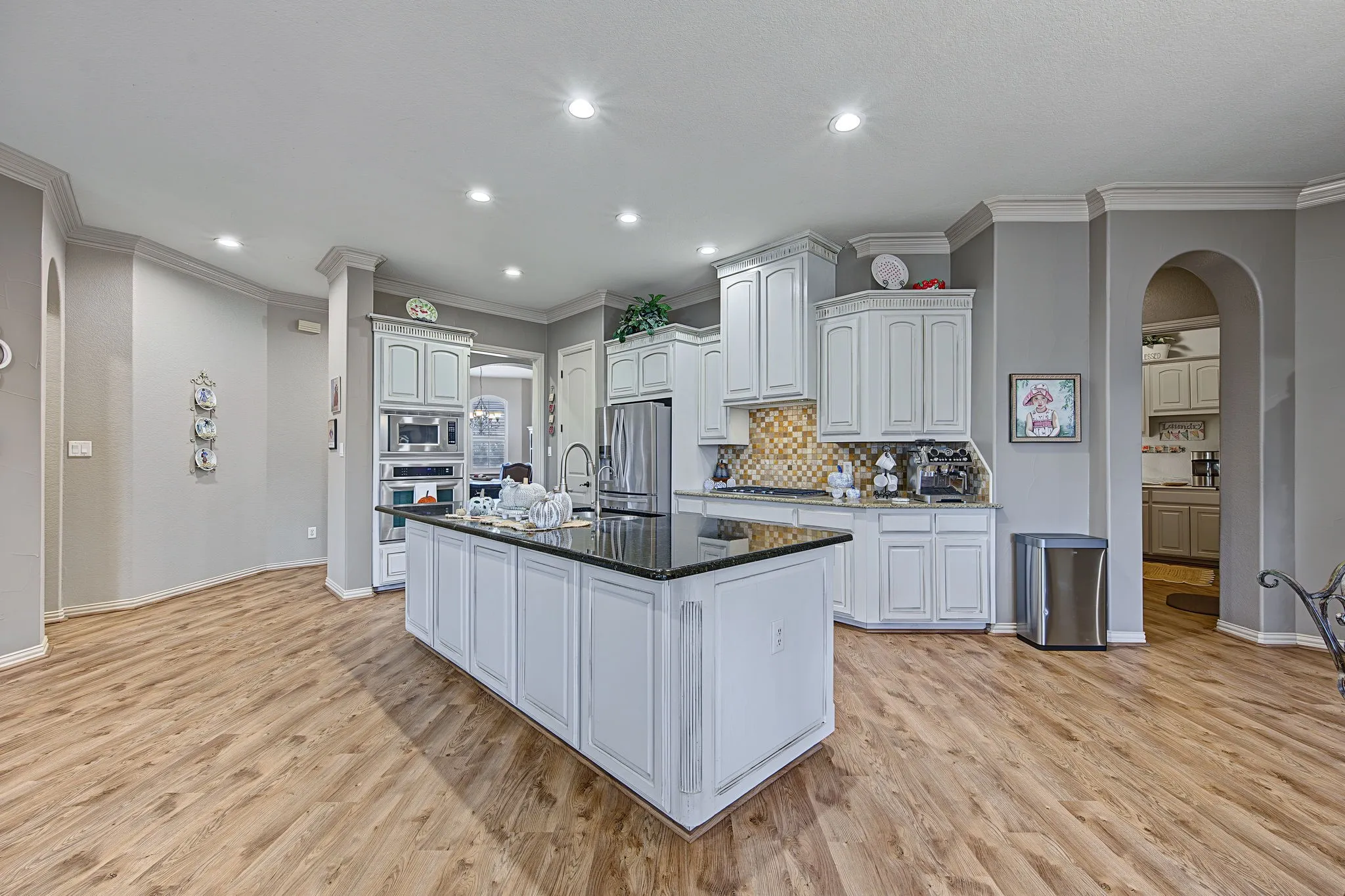 Kitchen featuring a large island with a dark countertop, white cabinetry with crown molding, a decorative tile backsplash, and wood-finish flooring