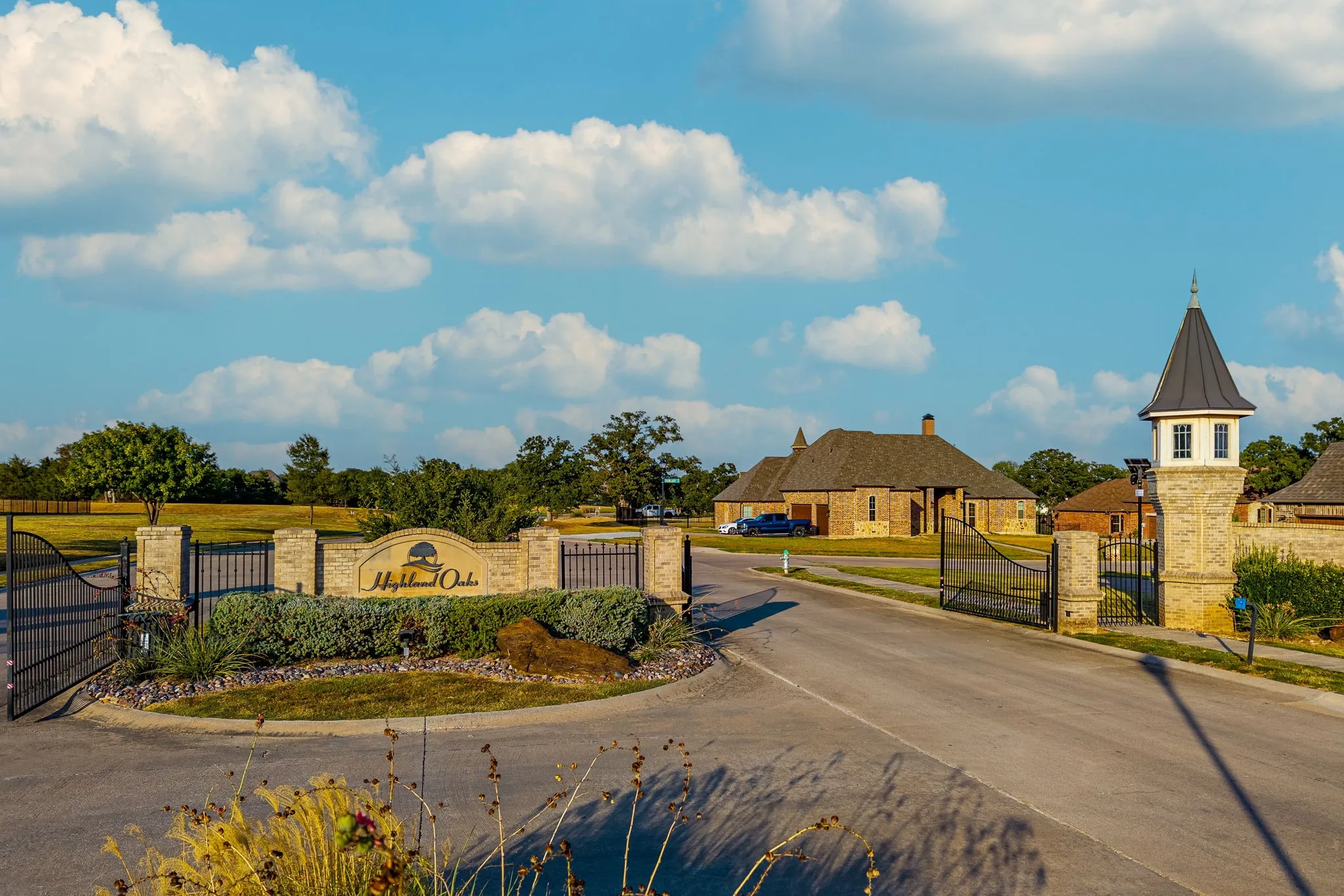 Gated community entrance featuring a stone monument with custom signage, wrought iron entry gates, and a decorative stone turret