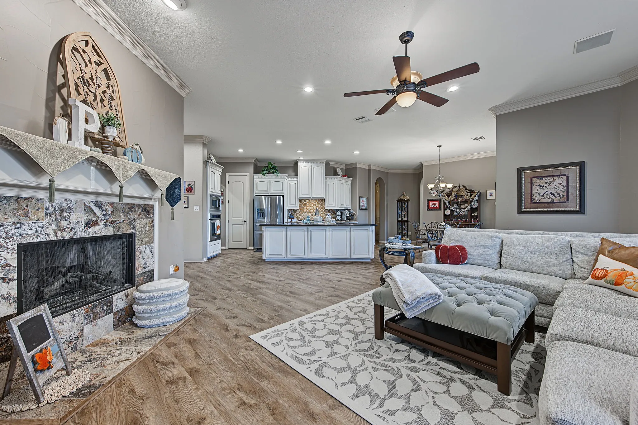 Wood-finish flooring throughout, tray ceiling with a built-in ceiling fan, recessed lighting, and a stone-clad fireplace with a hearth