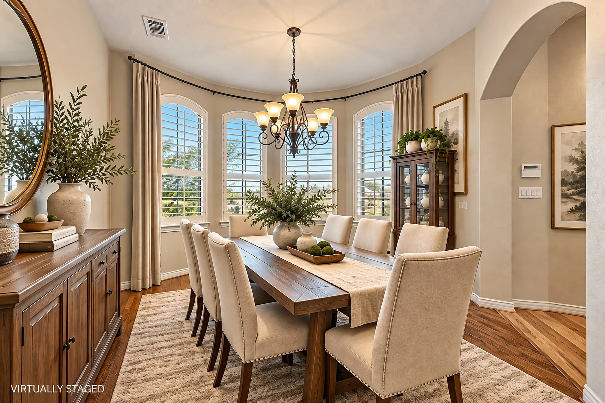 Virtually staged with modern transitional furniture. Recessed dining area with a curved wall of arched windows, wood-finish flooring, and an ornate chandelier