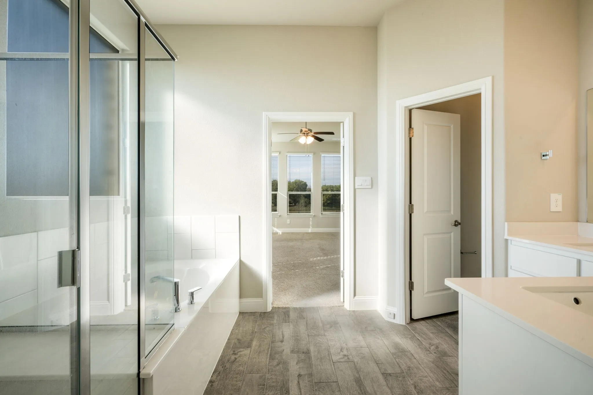Glass-enclosed shower, built-in soaking tub, wood-finish flooring, dual vanity with undermount sinks, and light-toned walls